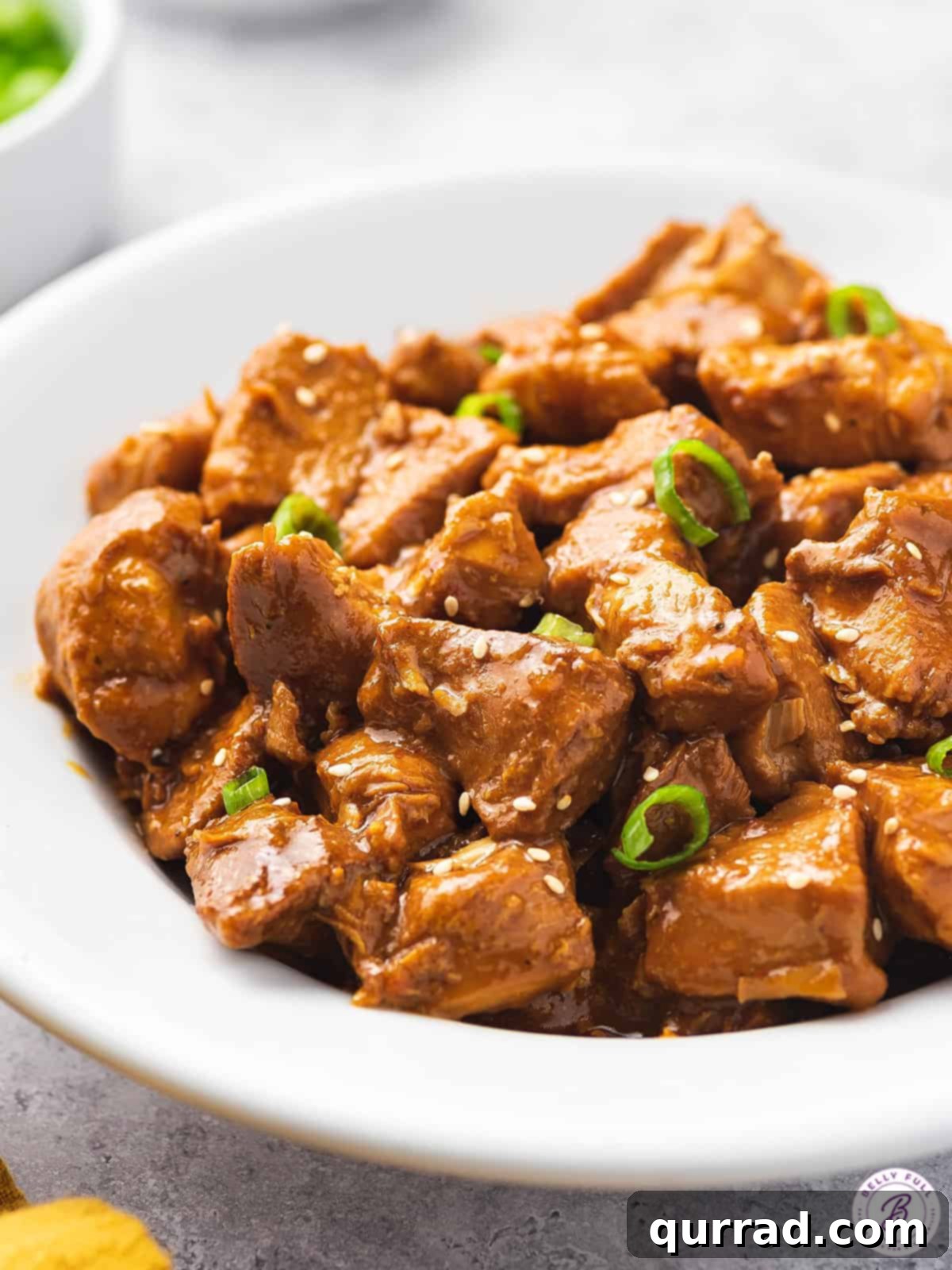 Slow cooker orange chicken in a white bowl, garnished with fresh green onions and sesame seeds