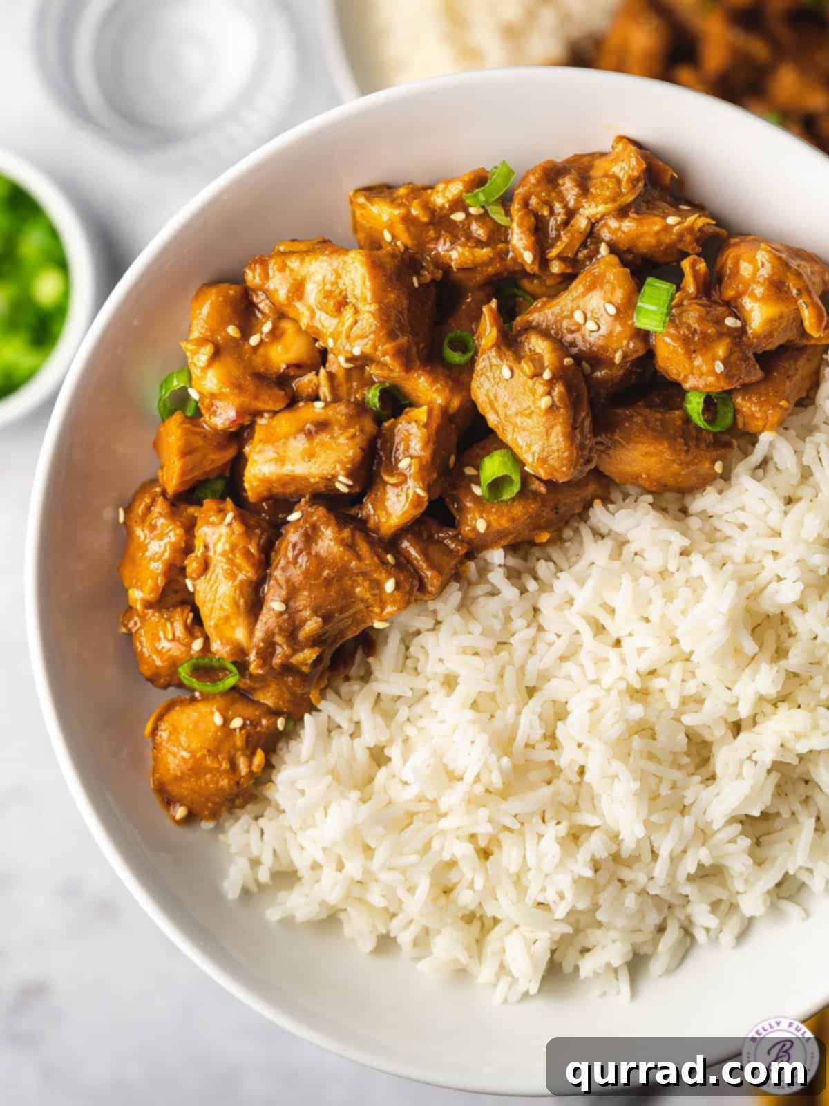 Overhead view of a bowl of orange chicken with rice, garnished generously with fresh scallions and sesame seeds