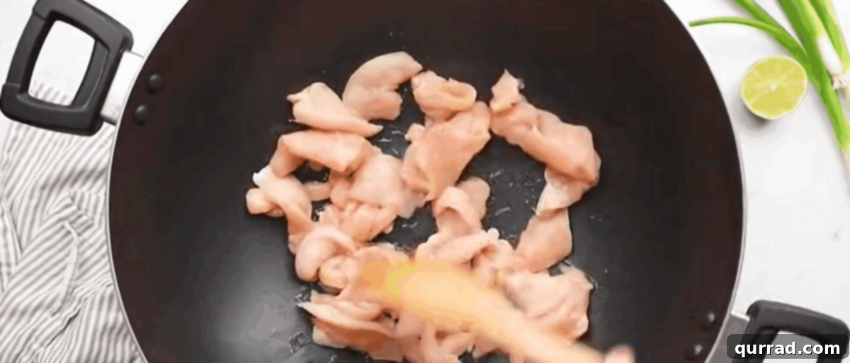 Chicken Pad Thai Perfection 5 Thinly sliced chicken breast pieces sizzling and browning in a hot wok with cooking oil.