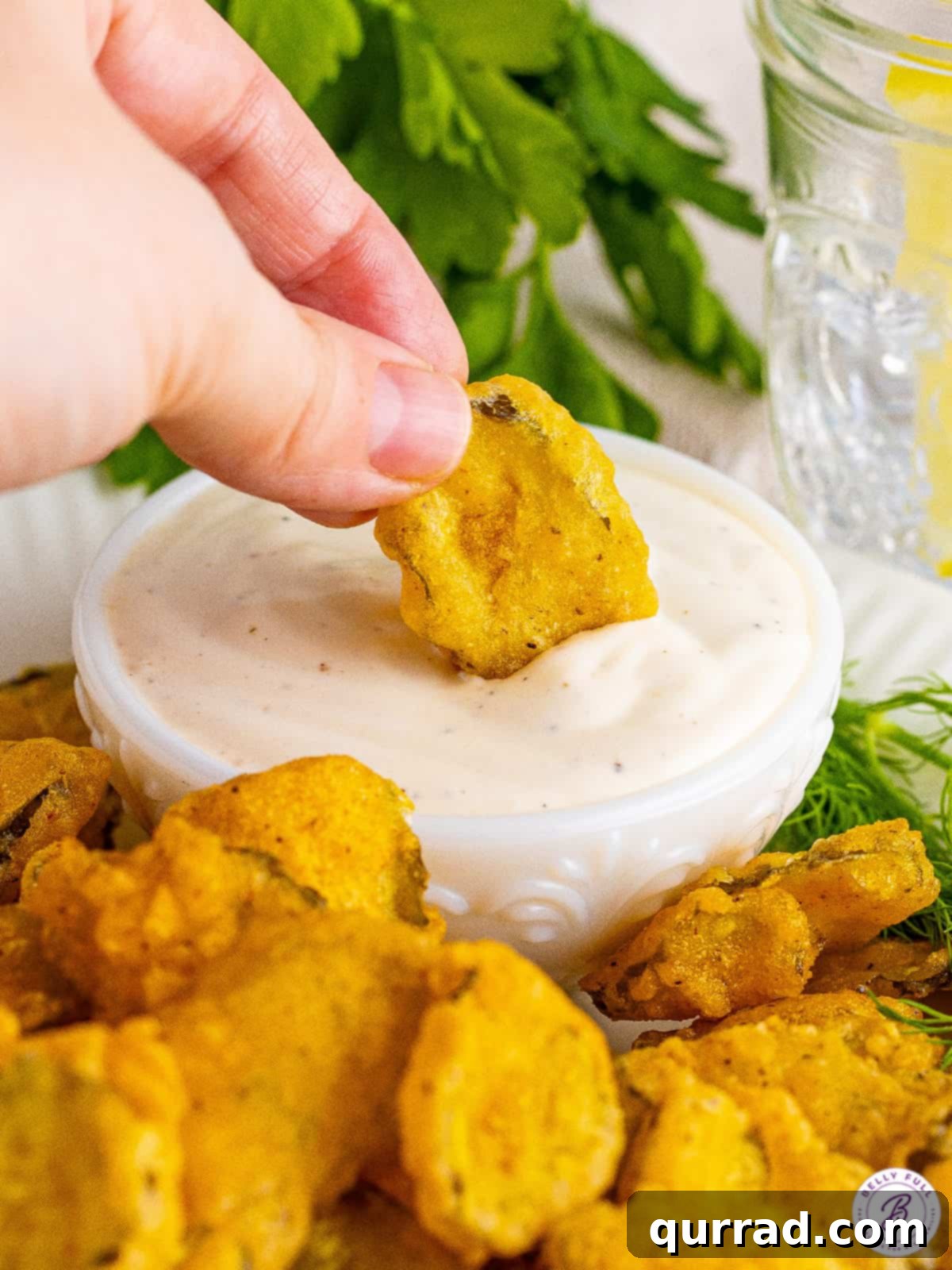 Dipping a Fried Pickle in Ranch A hand dipping a crispy fried pickle into a small white bowl of creamy ranch dressing, highlighting the perfect crunch.