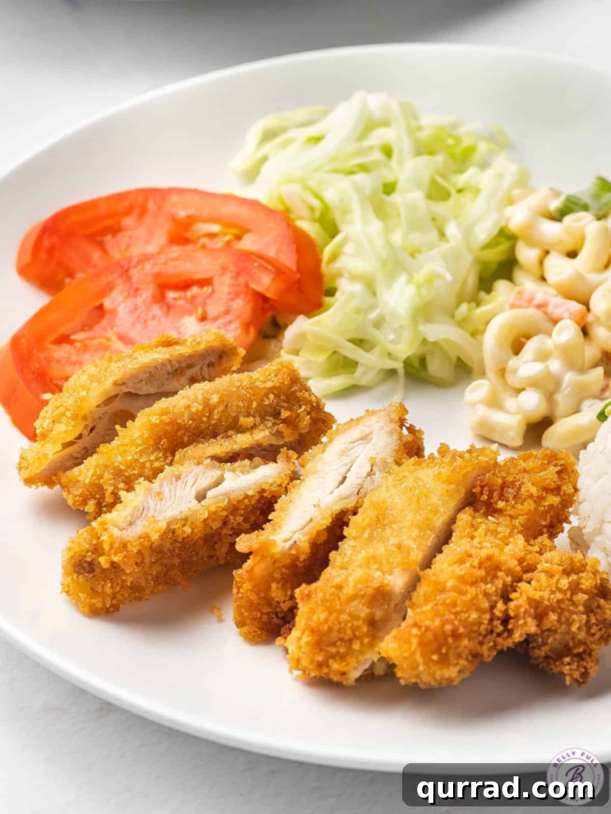 Panko-Crusted Chicken Katsu 2 Golden-fried Chicken Katsu on a plate, served with fresh tomatoes, shredded cabbage, and creamy macaroni salad.