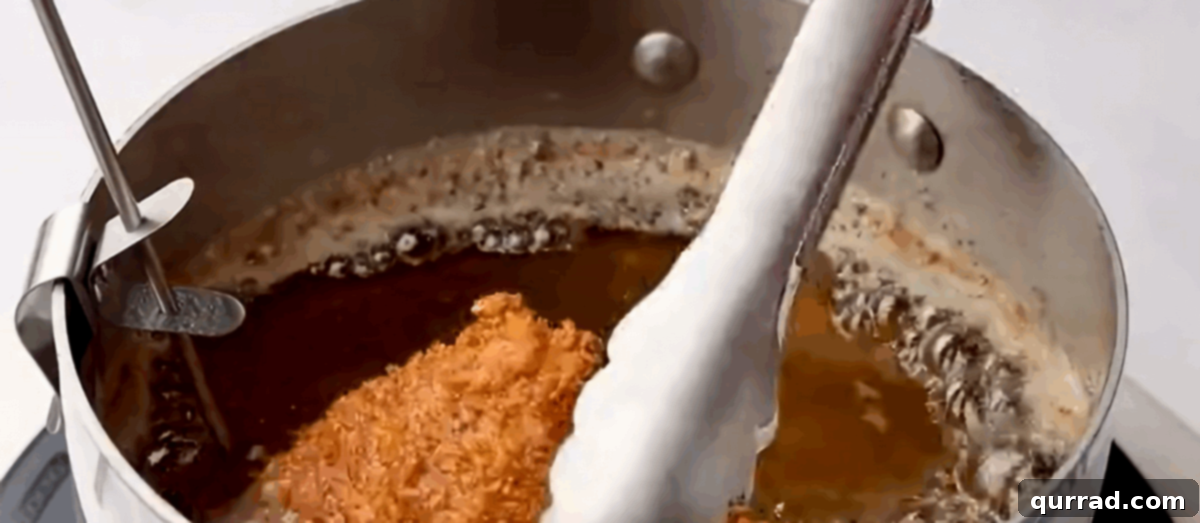 Panko-Crusted Chicken Katsu 7 A breaded chicken cutlet being deep-fried in hot oil, turning golden brown.