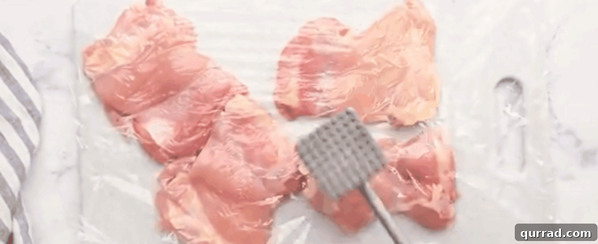 Panko-Crusted Chicken Katsu 4 Chicken thigh covered in plastic wrap being tenderized with a meat mallet to an even thickness.