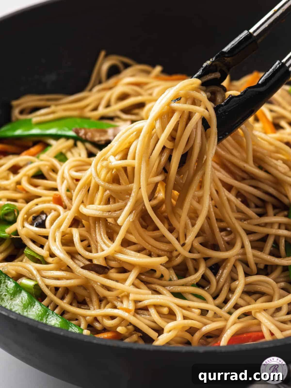 Perfectly Tossed Veggie Lo Mein Tongs stirring a fresh batch of veggie lo mein in a bowl.