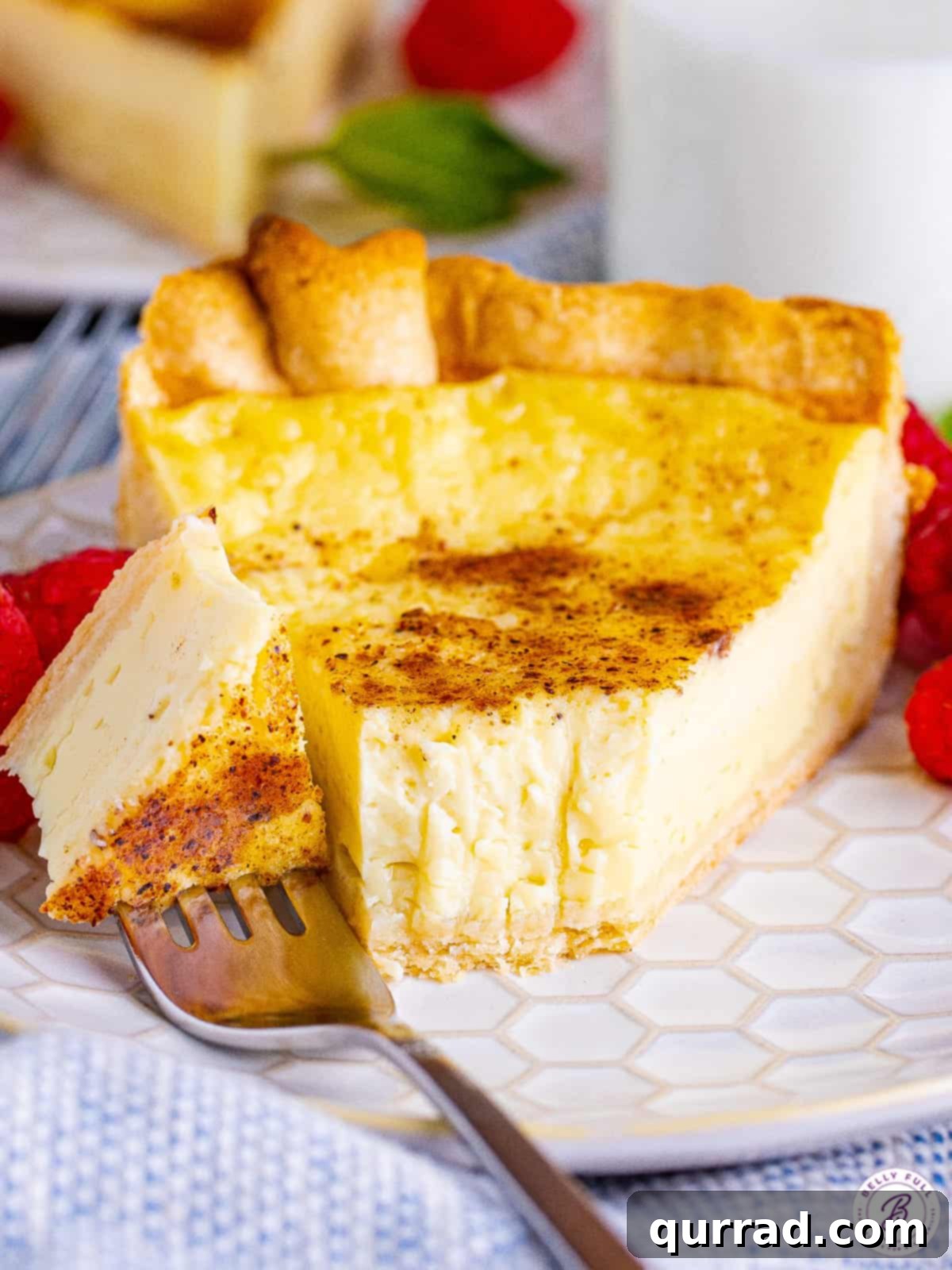 This Easy Custard Pie is a classic, simple dessert made with just 8 ingredients. The filling is incredibly rich and creamy, while not being too sweet. A slice of creamy custard pie on a white plate with a fork taking a bite, showing the perfect texture of the filling.