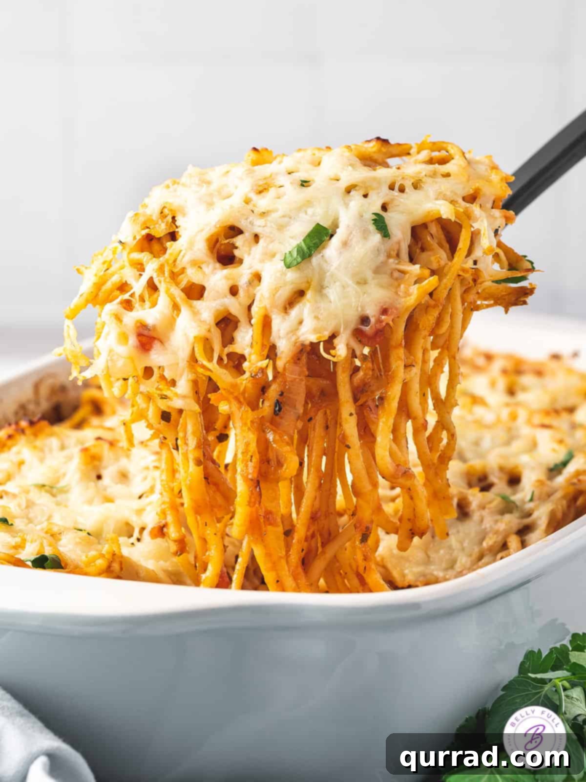 No pre-cooking needed! Just toss, add broth, and bake for amazing baked spaghetti. A spatula serving a portion of spaghetti bake, highlighting its cheesy and saucy texture.