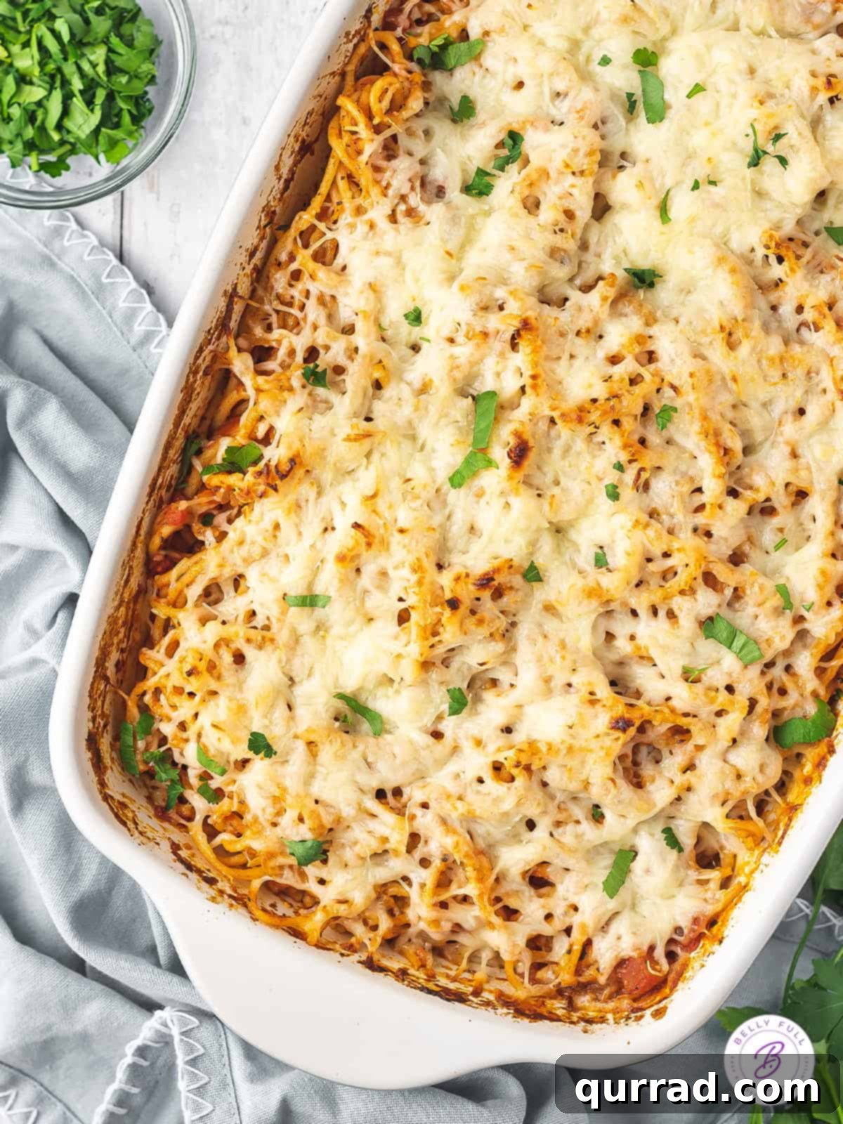No pre-cooking needed! Just toss, add broth, and bake for amazing baked spaghetti. Overhead view of baked spaghetti in a casserole dish with melted cheese and fresh parsley.