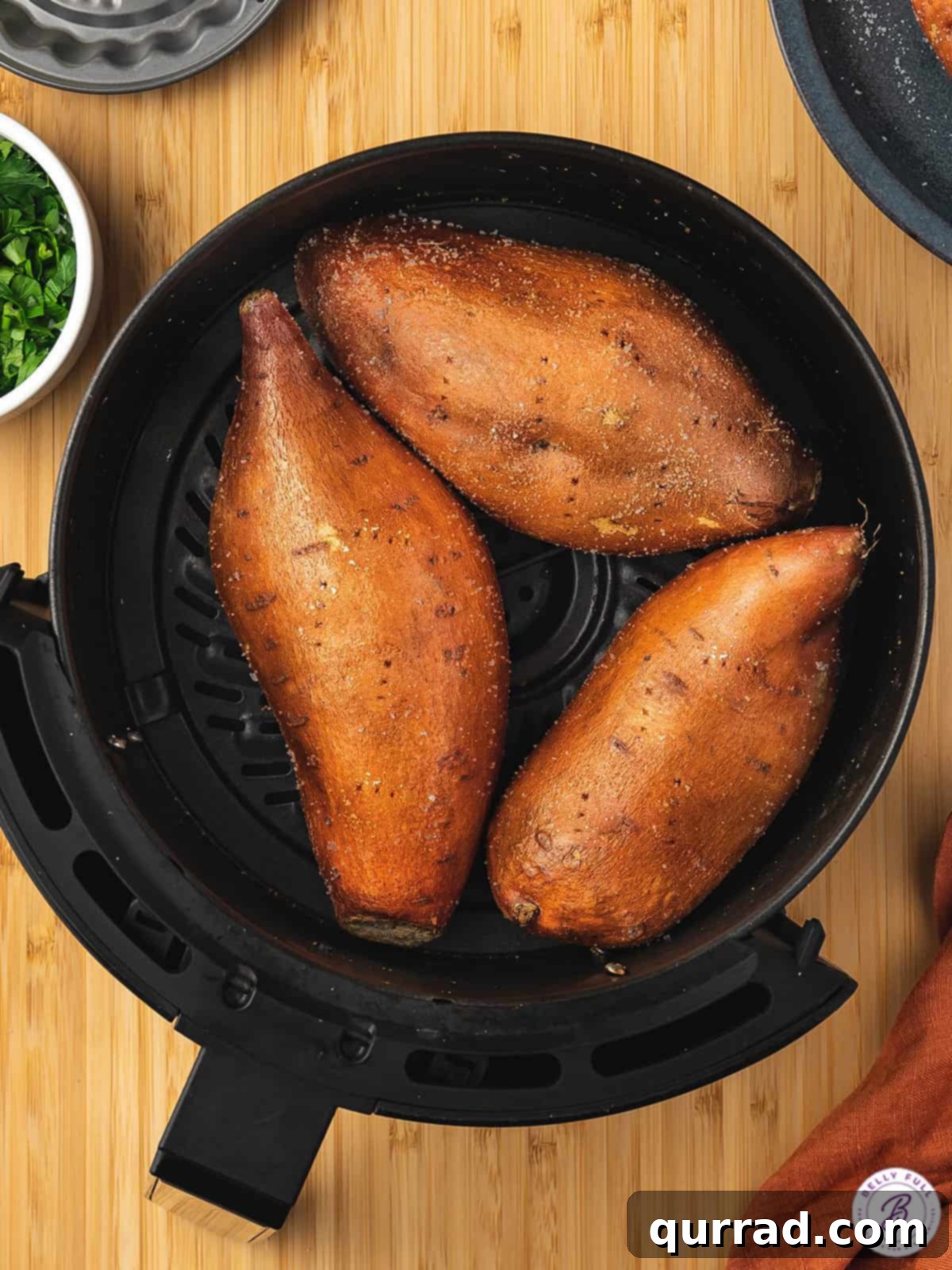 Three medium sweet potatoes neatly arranged in the basket of an air fryer, ready for cooking.