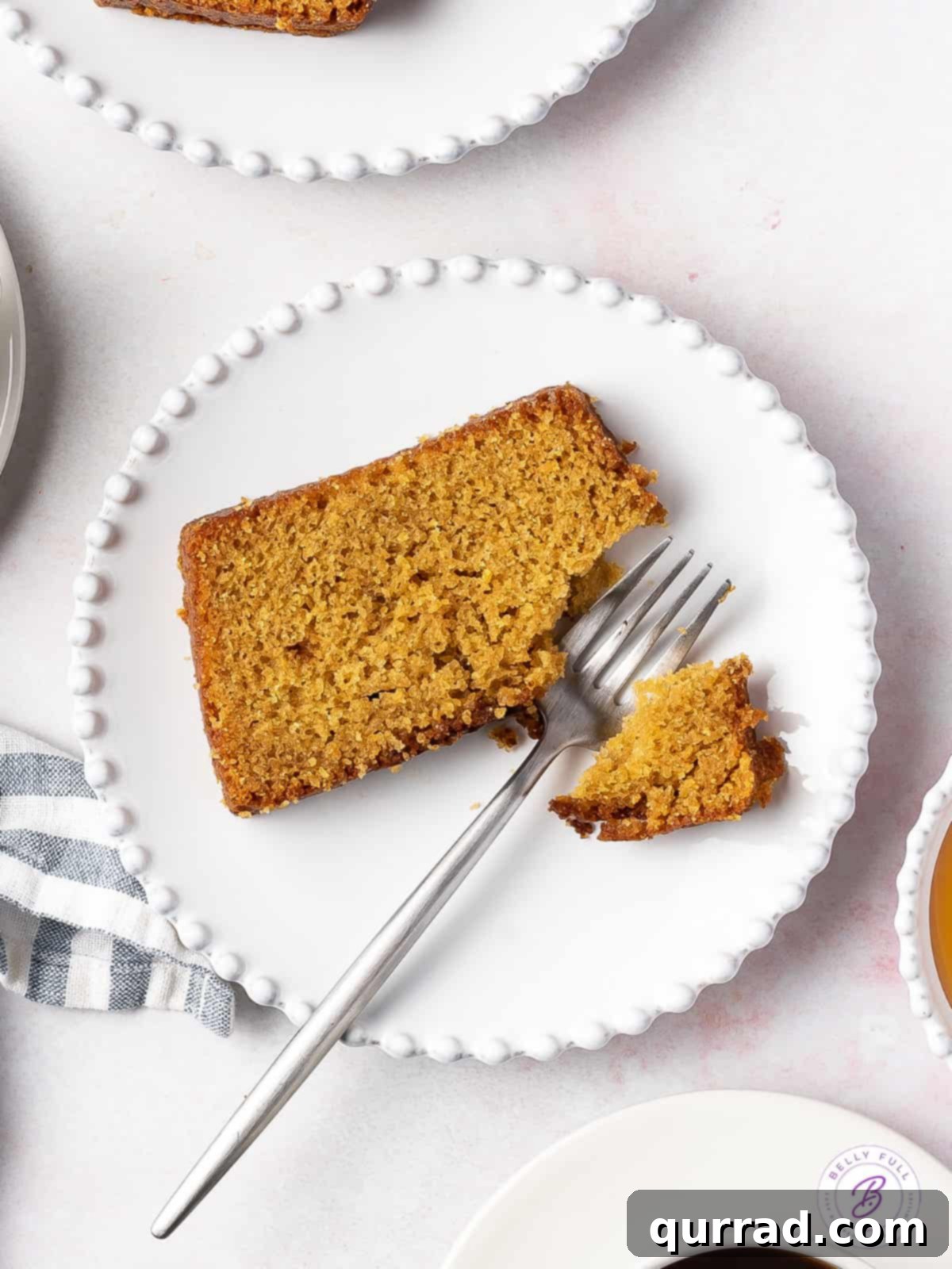 Discover the ultimate Moist, sweet, and subtly flavored Honey Cake – a traditional Rosh Hashanah dessert made with only 11 simple ingredients and prepared in under an hour. A perfect treat for any time of the year! Overhead shot of a perfect slice of honey cake on a white plate, with a fork resting beside it, inviting a taste.