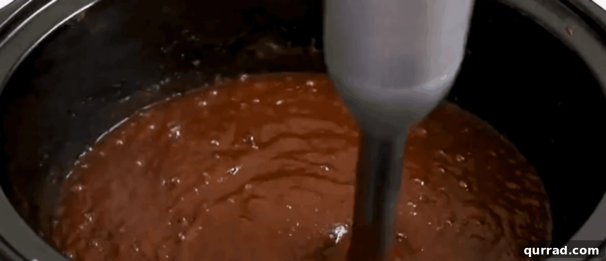 Velvety Slow Cooker Apple Butter 4 An immersion blender being used to puree the softened apples directly in the slow cooker, creating a smooth and creamy apple butter consistency.