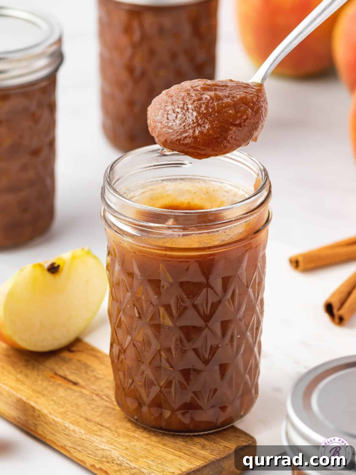 Enjoy your homemade Slow Cooker Apple Butter on your favorite morning treats or as a delicious gift. A glistening spoon held above an open mason jar filled with freshly made slow cooker apple butter, highlighting its smooth, rich texture and inviting color.