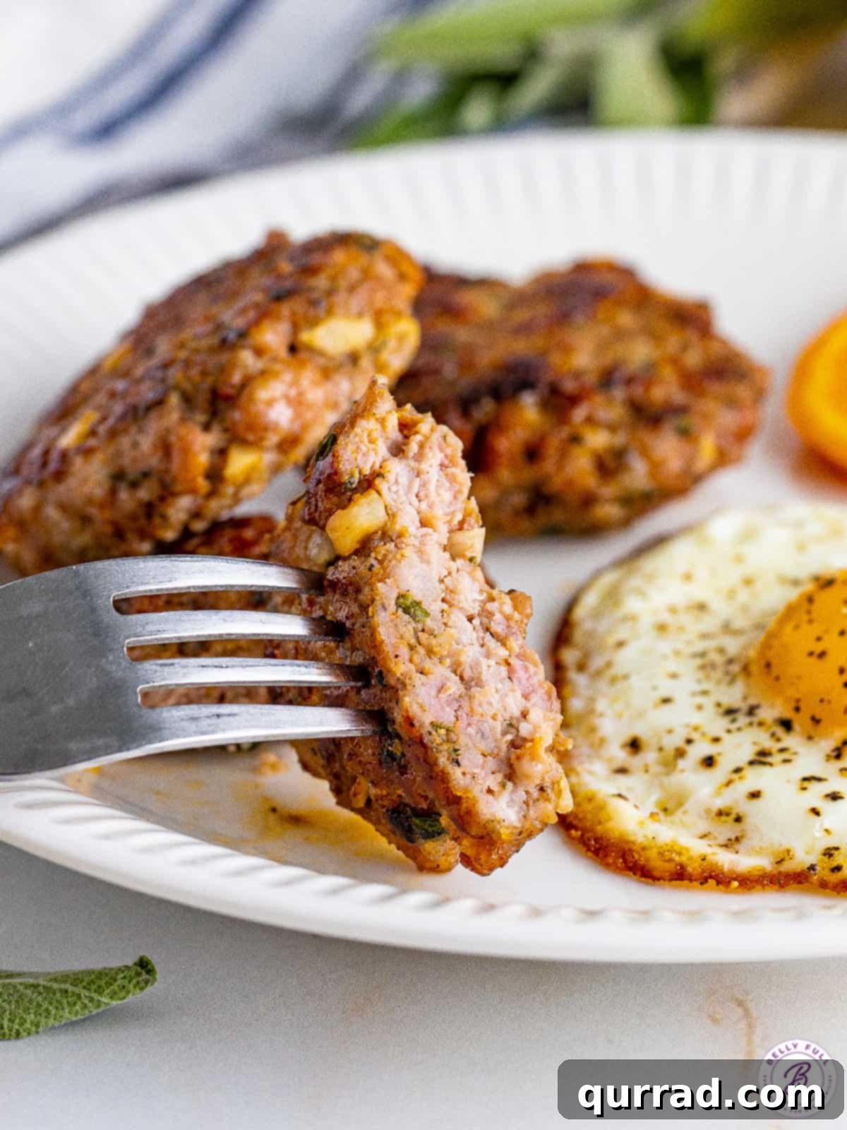 A fork in a piece of breakfast sausage on a plate with an egg