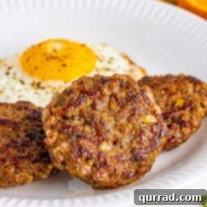 Three breakfast sausage patties on a white plate with a fried egg