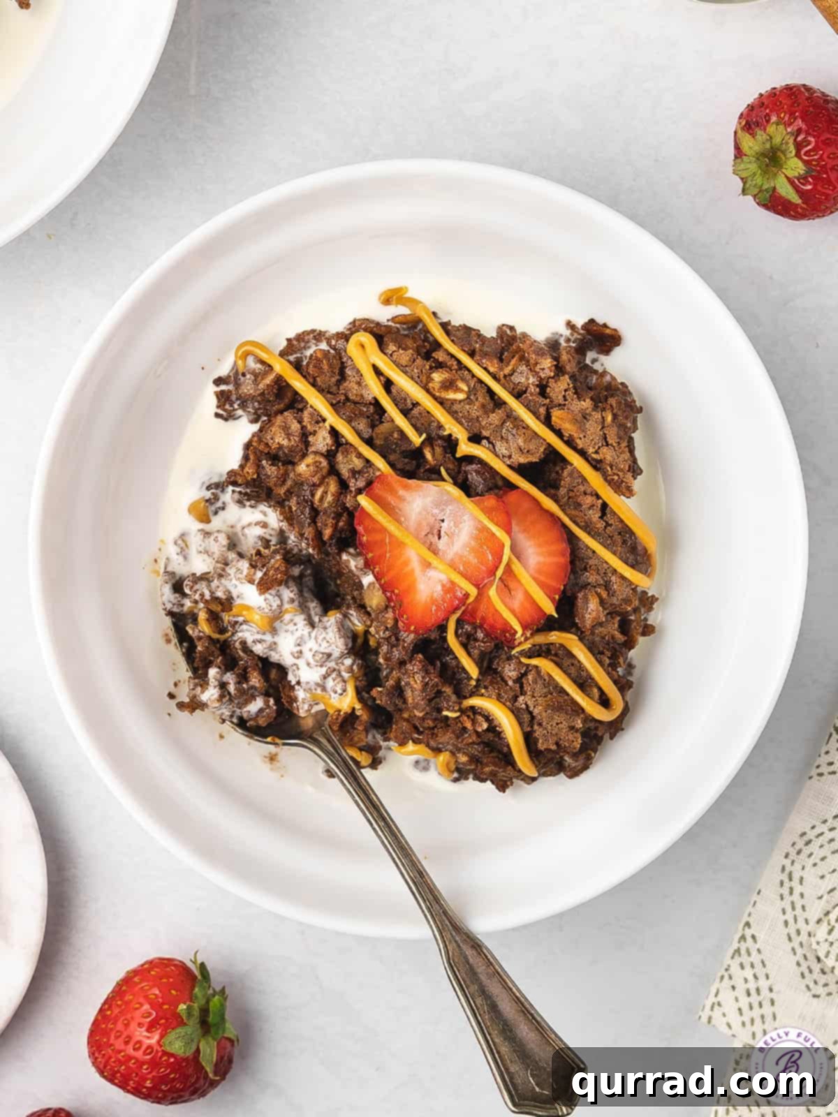 A close-up of brownie baked oatmeal topped generously with creamy peanut butter and vibrant sliced strawberries, emphasizing its delicious and wholesome toppings.