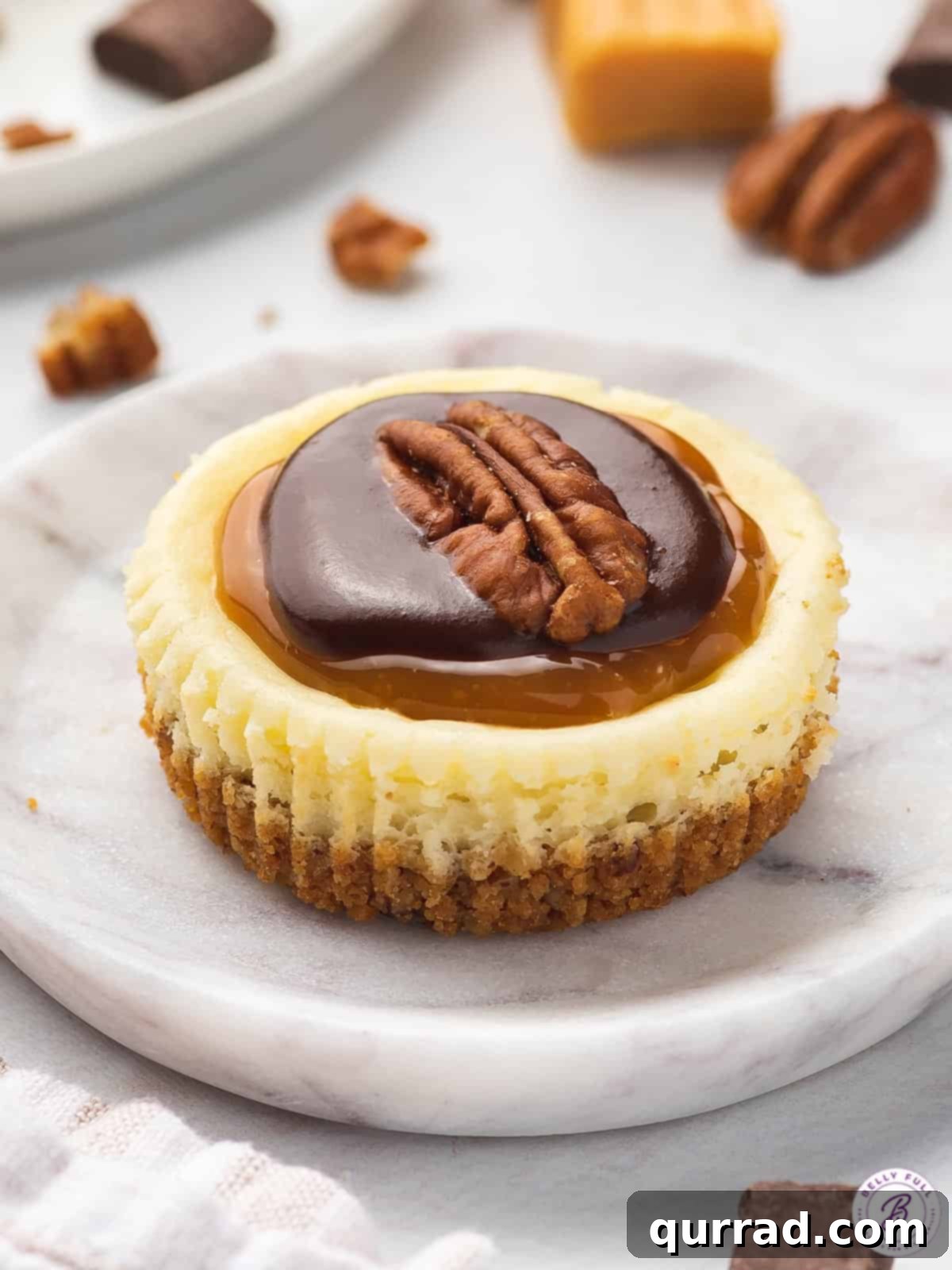 Topped with caramel, chocolate, and pecans these Mini Turtle Cheesecakes are a spin off the traditional candy. Easy to make & no water bath! Angled view of a mini turtle cheesecake on a marble plate