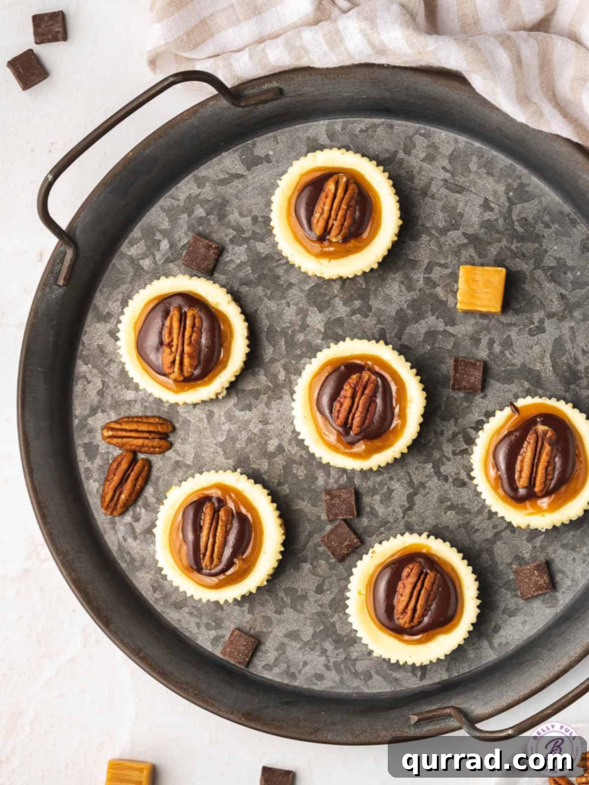 Topped with caramel, chocolate, and pecans these Mini Turtle Cheesecakes are a spin off the traditional candy. Easy to make & no water bath! Overhead view of mini turtle cheesecakes on a metal plate