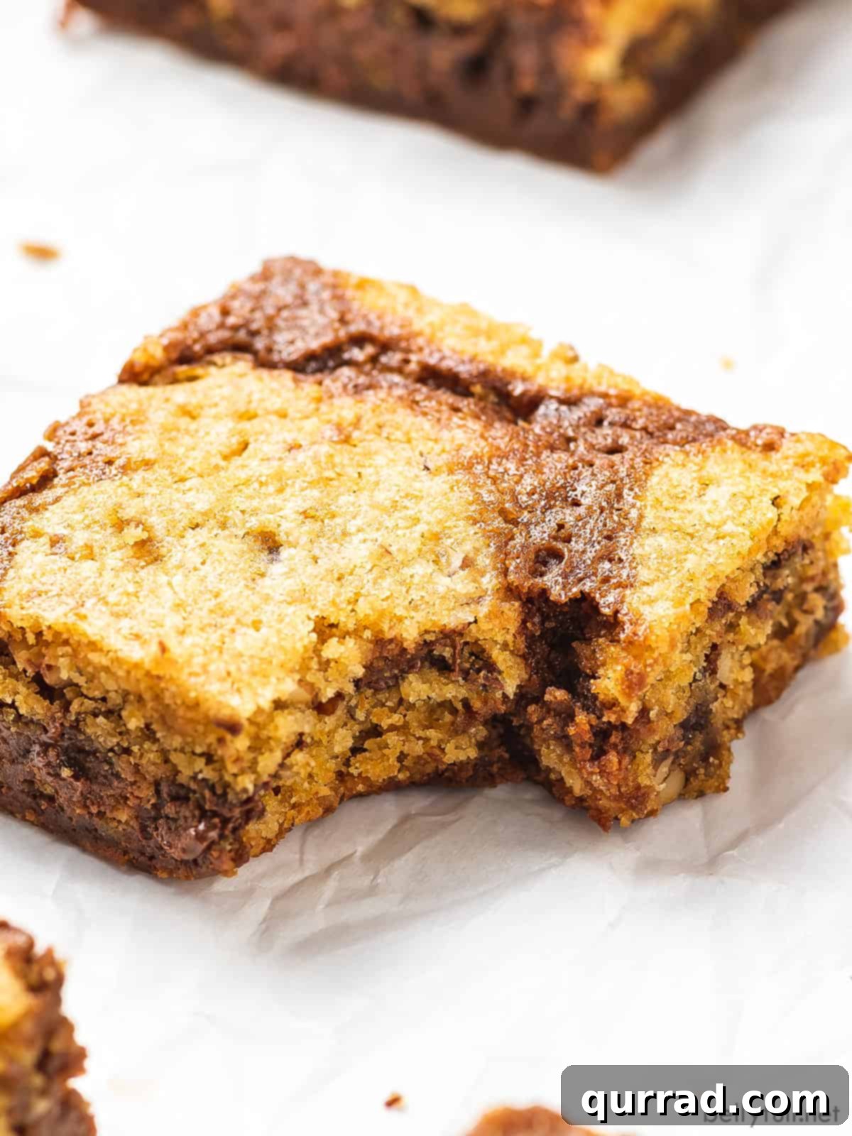 Fudgy brownies topped with chewy chocolate chip cookies, these Brookies are made completely from scratch in under an hour. A brookie on a white plate with a corner bite taken out, showing the layers and texture, along with melted chocolate chips.