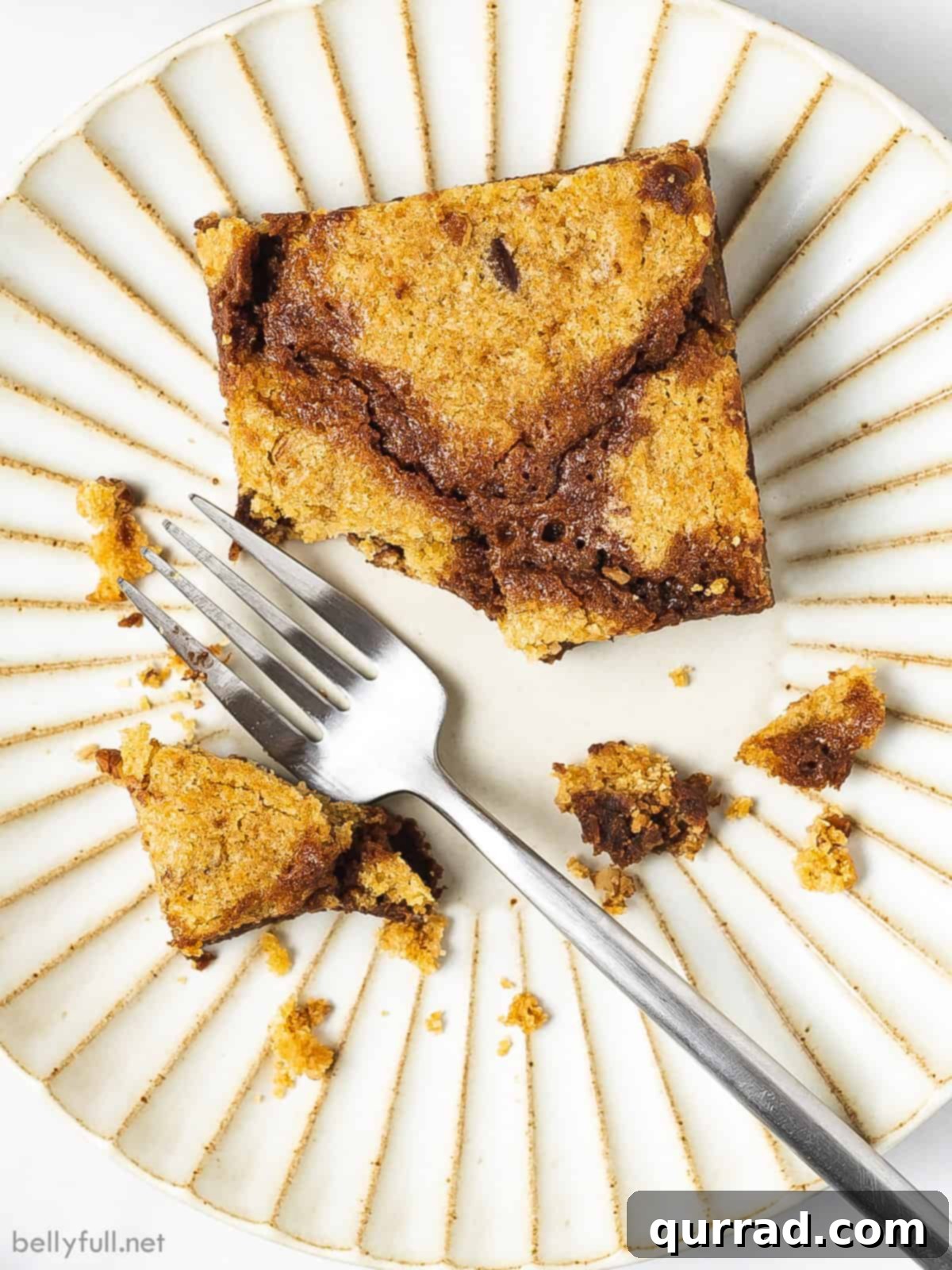 Fudgy brownies topped with chewy chocolate chip cookies, these Brookies are made completely from scratch in under an hour. Overhead view of a single brookie bar on a white plate with a fork, showing its rich, layered texture and inviting crumb.