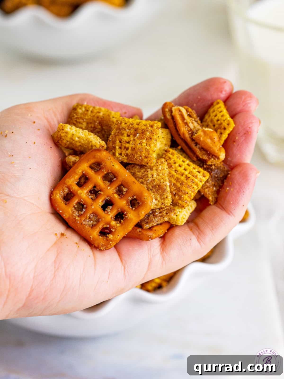 Cinnamon Sugar Chex Mix is an addictive party snack mix with a crunchy and sweet cinnamon coating. Great for gift-giving! A hand holds a generous portion of freshly made cinnamon sugar Chex mix, showcasing its irresistible crunch.