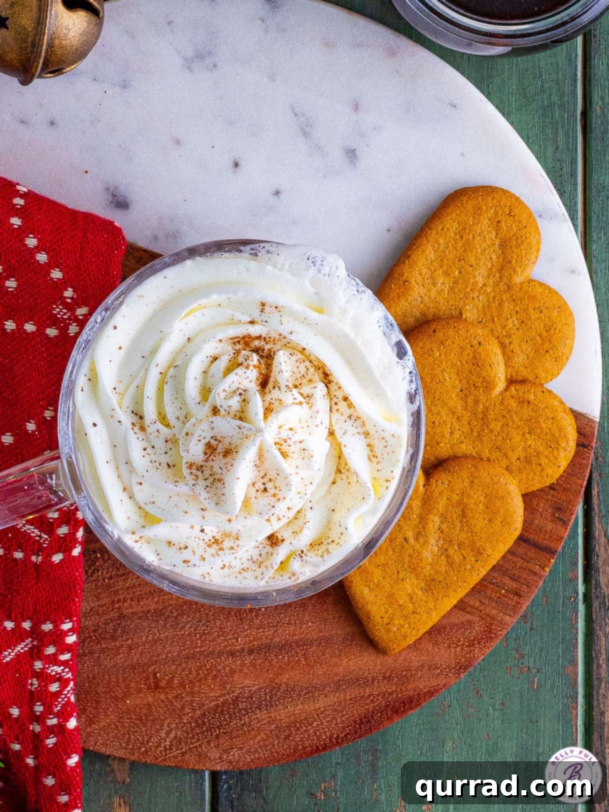 Espresso is sweetened with homemade gingerbread syrup and topped with frothed milk and whipped cream in this Gingerbread Latte recipe. Overhead view of a gingerbread latte next to heart-shaped cookies, emphasizing a cozy winter scene