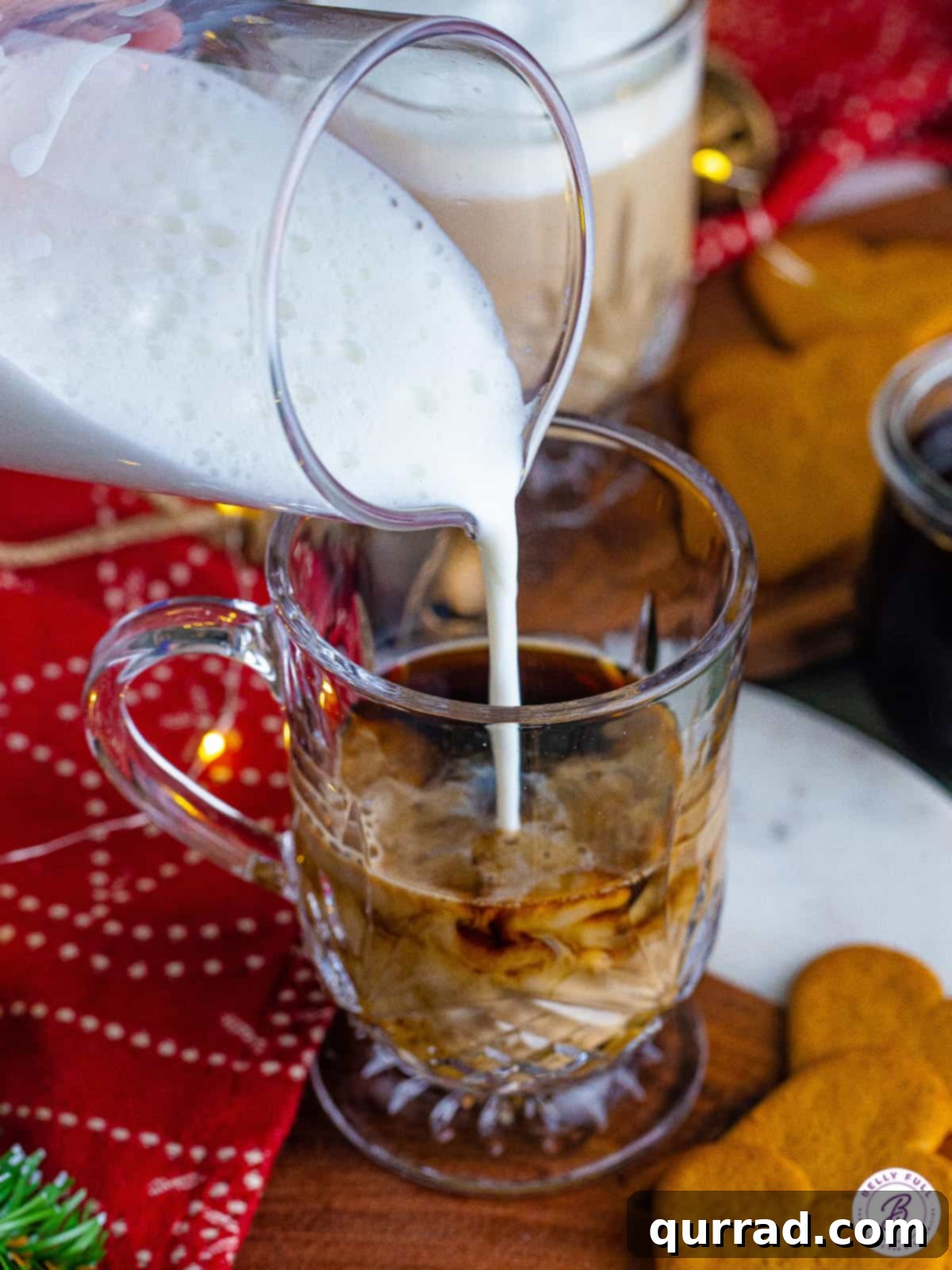 Espresso is sweetened with homemade gingerbread syrup and topped with frothed milk and whipped cream in this Gingerbread Latte recipe. Frothed milk being poured over espresso and gingerbread syrup in a clear mug