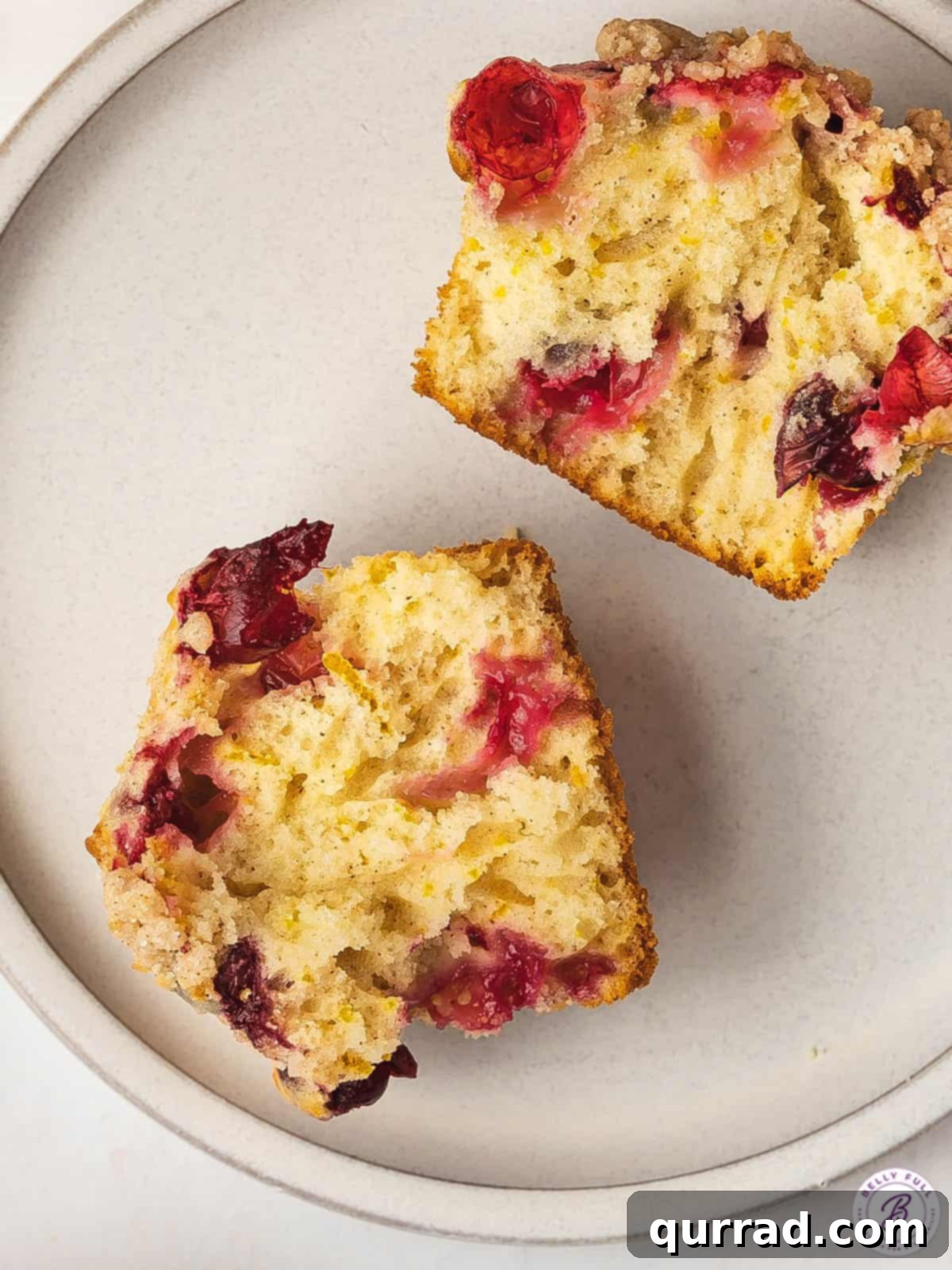 Made with tart cranberries, orange zest, and orange juice, these Cranberry Orange Muffins are bursting with flavor. Fluffy & moist! Overhead view of a cranberry orange muffin cut in half on a plate