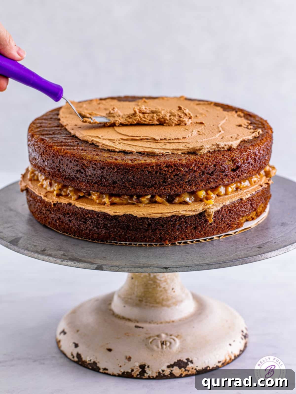 Chocolate buttercream being spread on a chocolate cake layer, preparing for the next layer of frosting. A spatula smoothing luscious chocolate buttercream over a baked chocolate layer cake, mid-assembly.