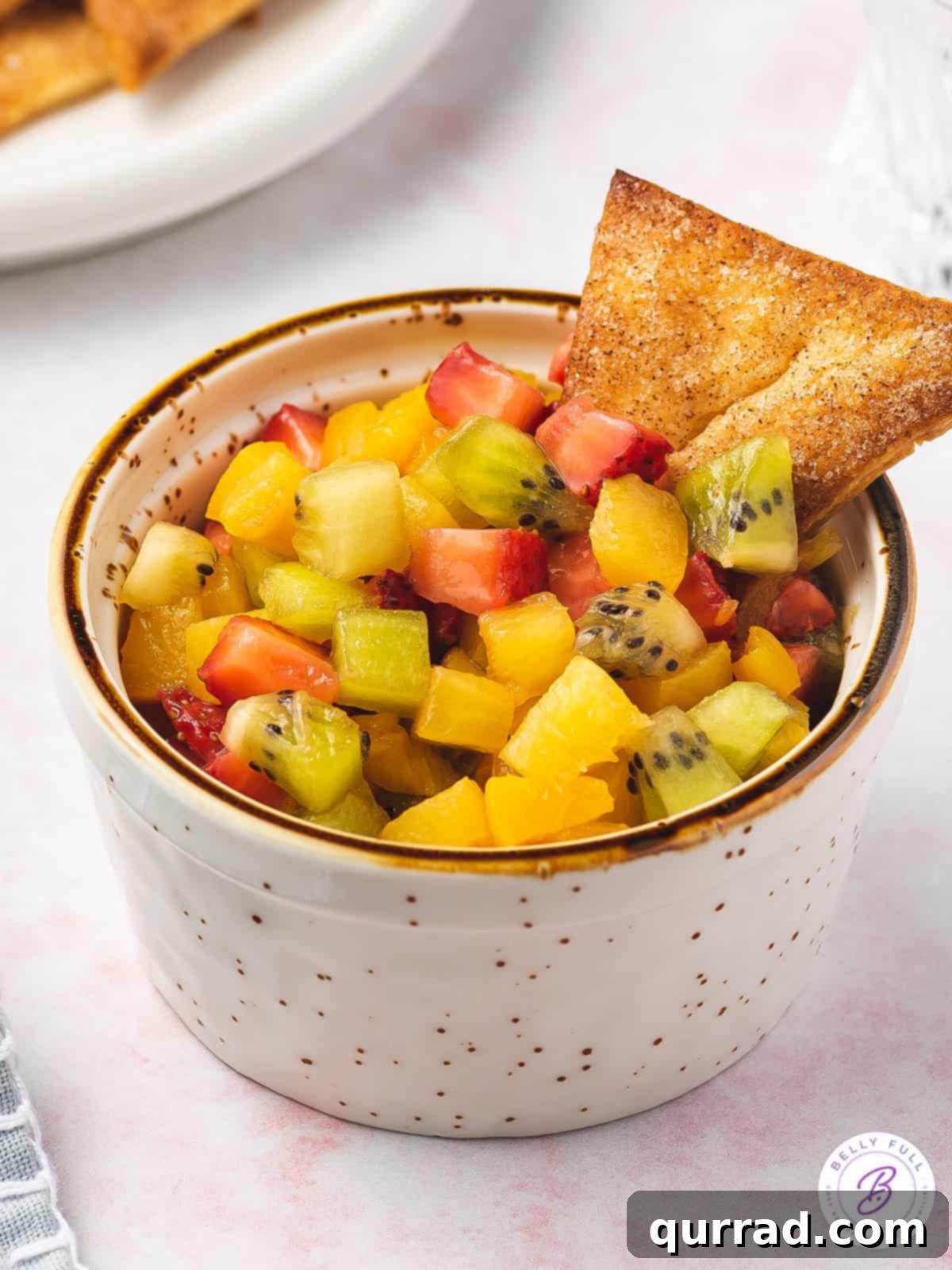 Fruit Salsa and Pie Crust Chips 6 A bowl of colorful diced summer fruit salsa with a single cinnamon triangle pie crust chip, showcasing the perfect pairing.