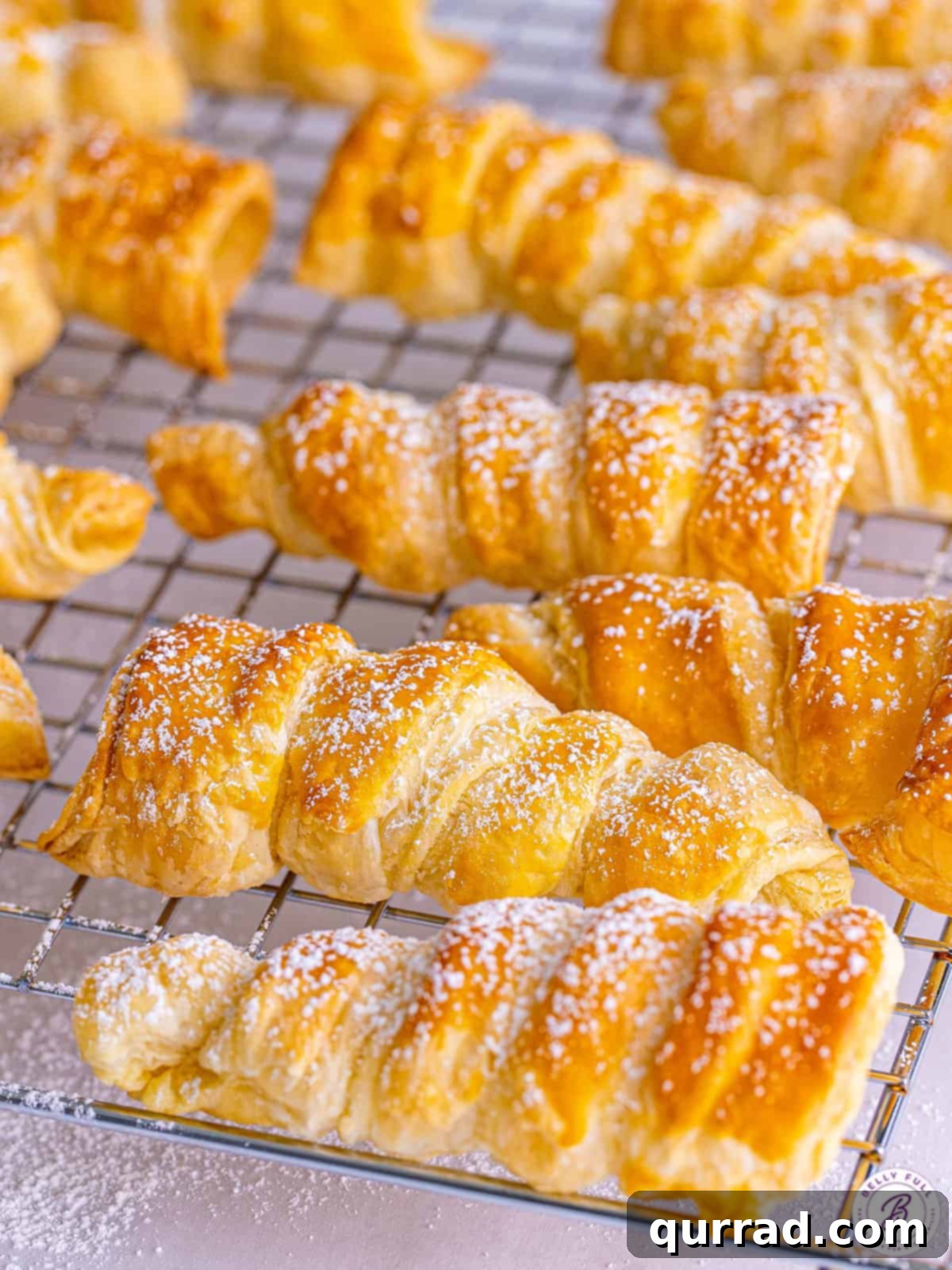 Cream horn shells on a cooling rack, sprinkled with icing sugar, ready for filling.