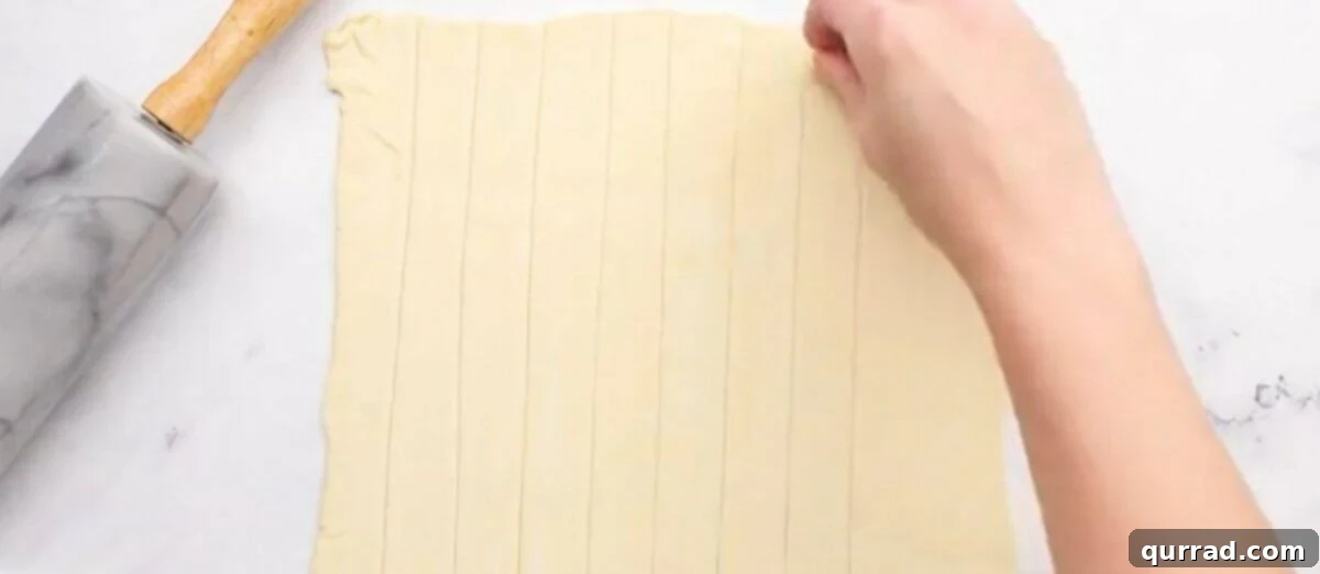Cutting the pastry into strips on a cutting board, demonstrating precision for uniform cream horns.