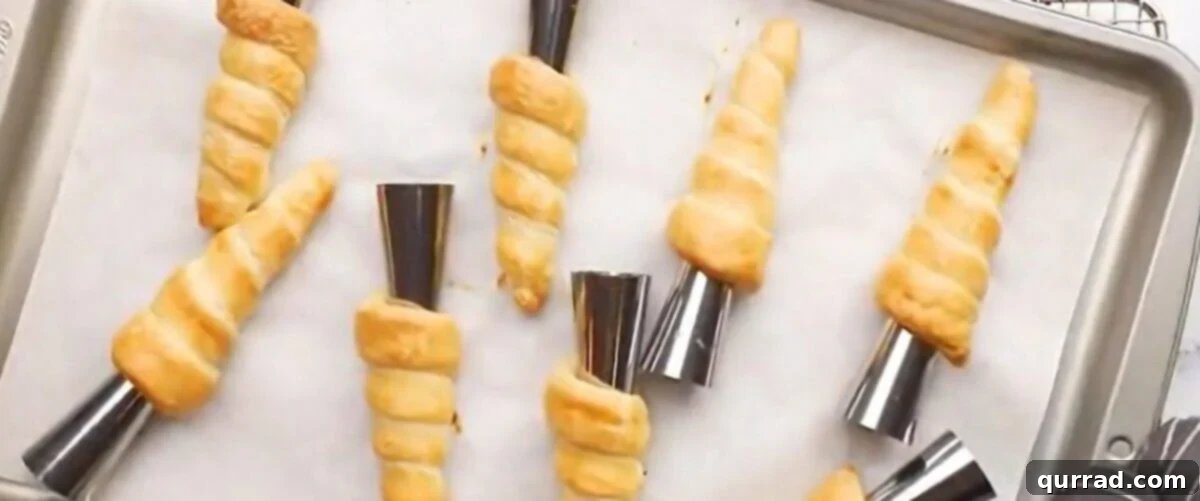 Baked creamed horns on a baking sheet on a cooling rack, showcasing their puffed, golden appearance.