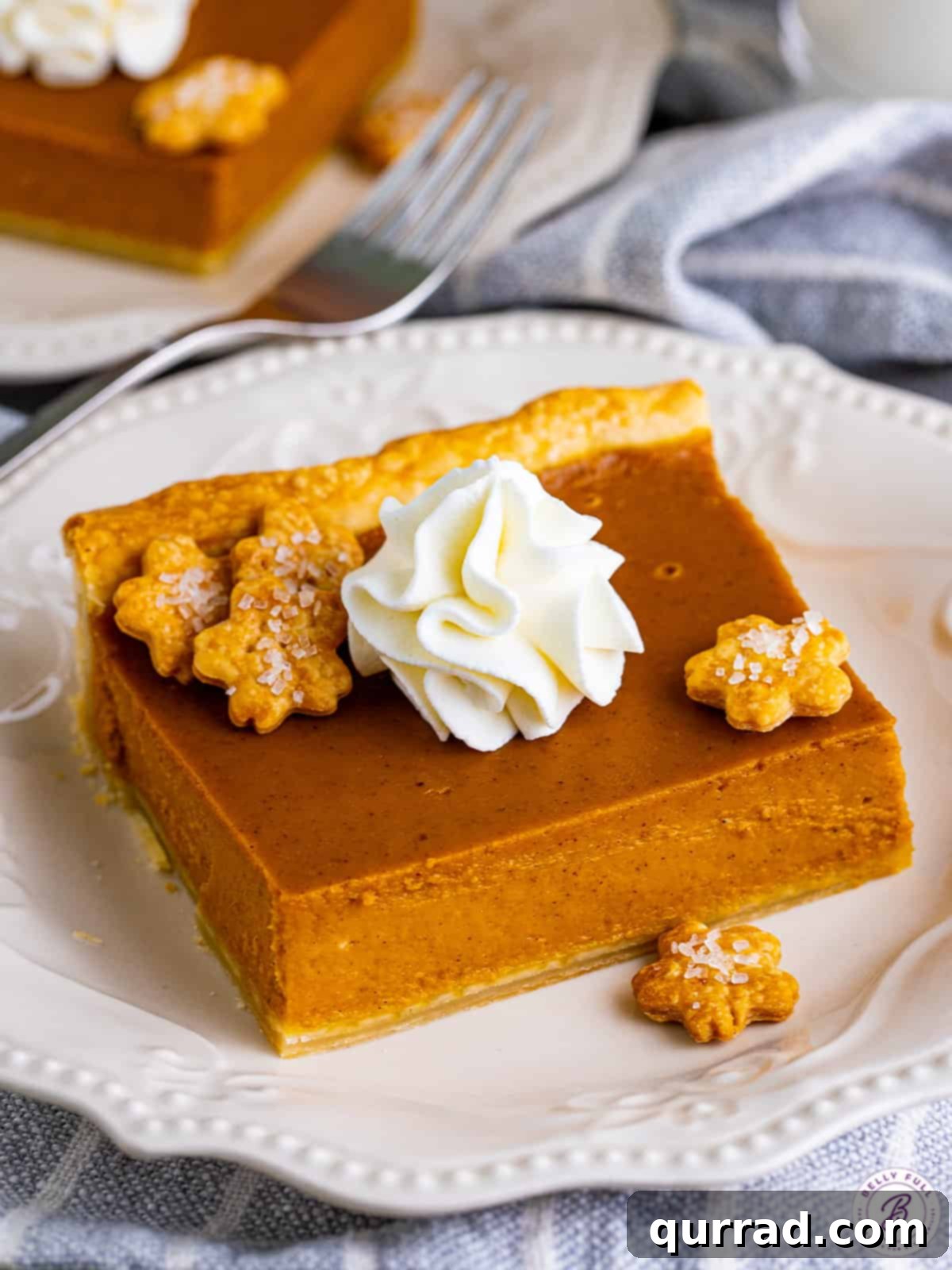 This Easy Pumpkin Slab Pie is the ultimate, foolproof Thanksgiving dessert, boasting a smooth, spiced filling that's simple to slice and serve. An inviting angled overhead view of a perfectly sliced piece of Pumpkin Slab Pie resting on a pristine white plate, showcasing its smooth texture and golden crust.