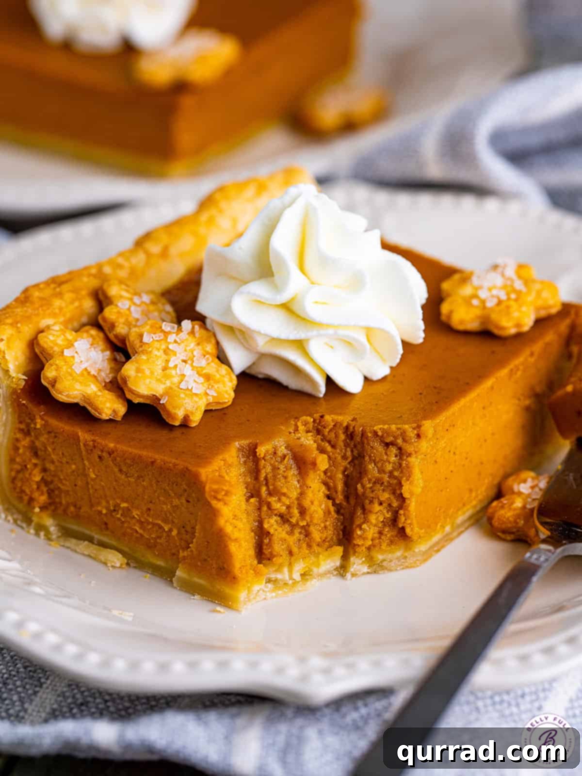 Savor every bite of this easy Pumpkin Slab Pie, a truly irresistible Thanksgiving dessert. An inviting angled view of a slice of pumpkin slab pie on a white plate, with a small bite missing, highlighting its deliciousness.