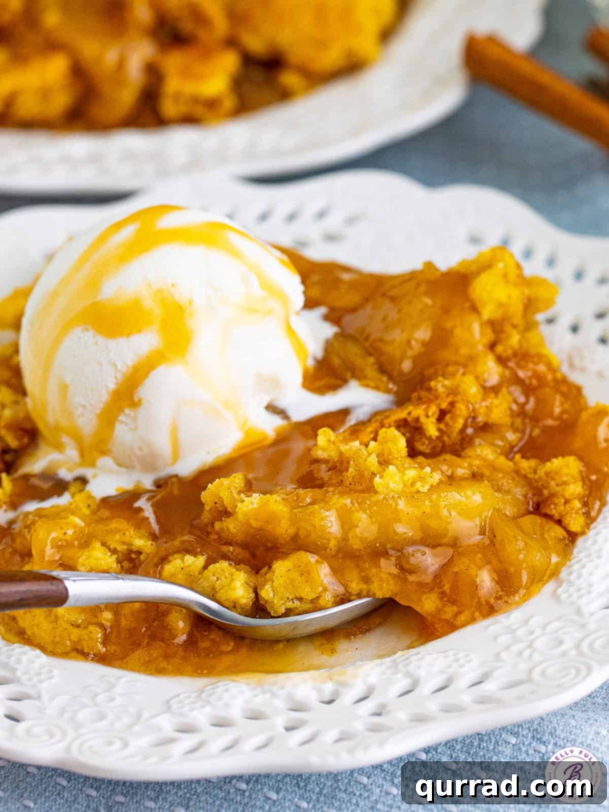 Irresistible Caramel Apple Dump Cake 7 A freshly baked caramel apple dump cake, glistening with caramel and topped with a melting scoop of vanilla ice cream, served on a pristine white plate.