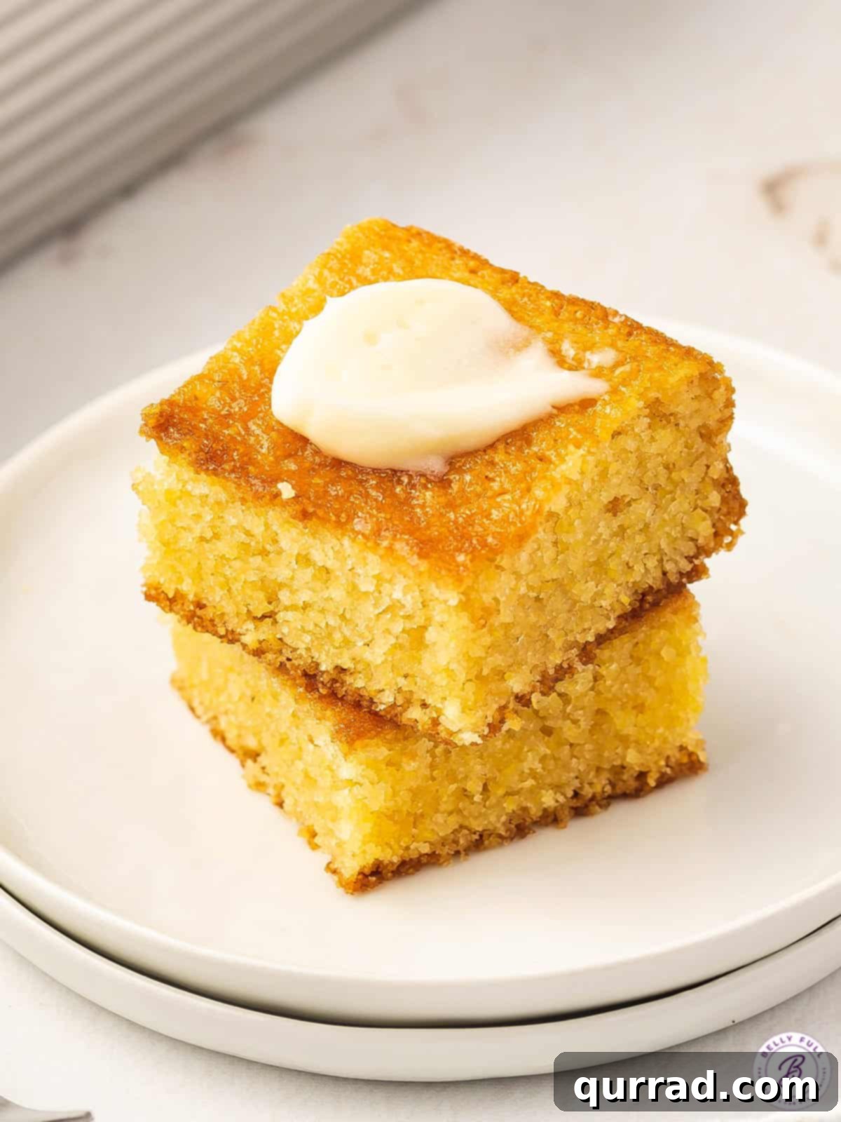 Two stacked squares of brown sugar cornbread with a pat of butter melting on top