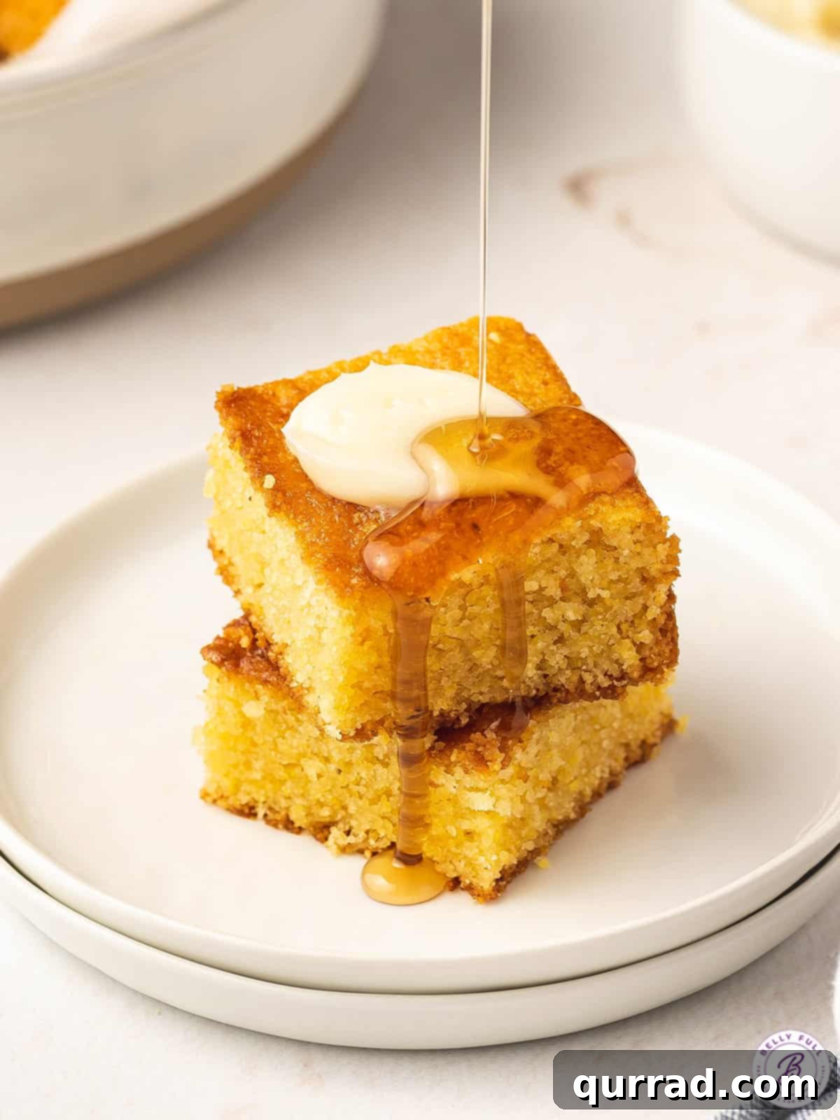 Two stacked squares of brown sugar cornbread with honey being drizzled on top