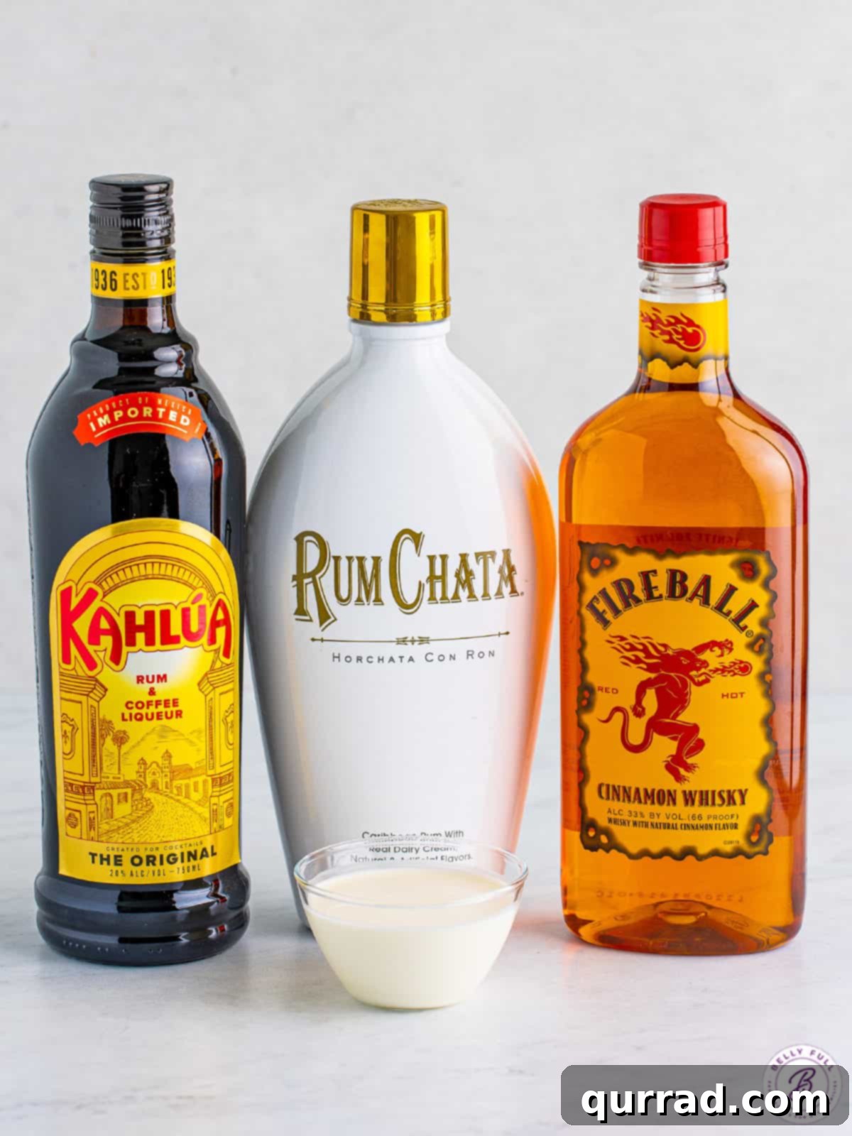 Bottles of Kahlua, Rumchata, and Fireball next to a bowl of heavy cream, key ingredients for the cocktail.