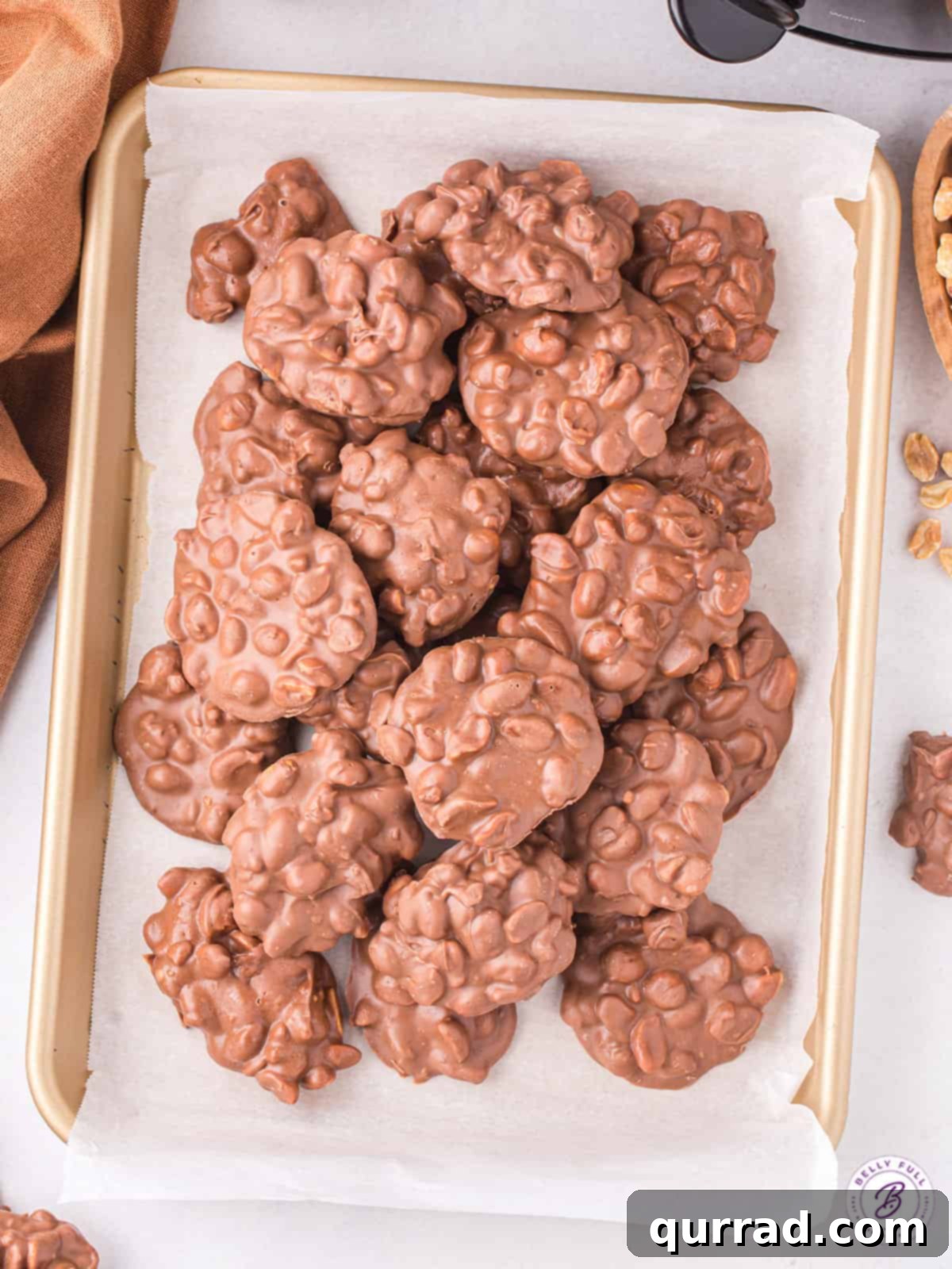 Crockpot Candy clusters hardening on parchment paper, showcasing their perfect form. Freshly made chocolate peanut clusters laid out on parchment paper to cool and set.