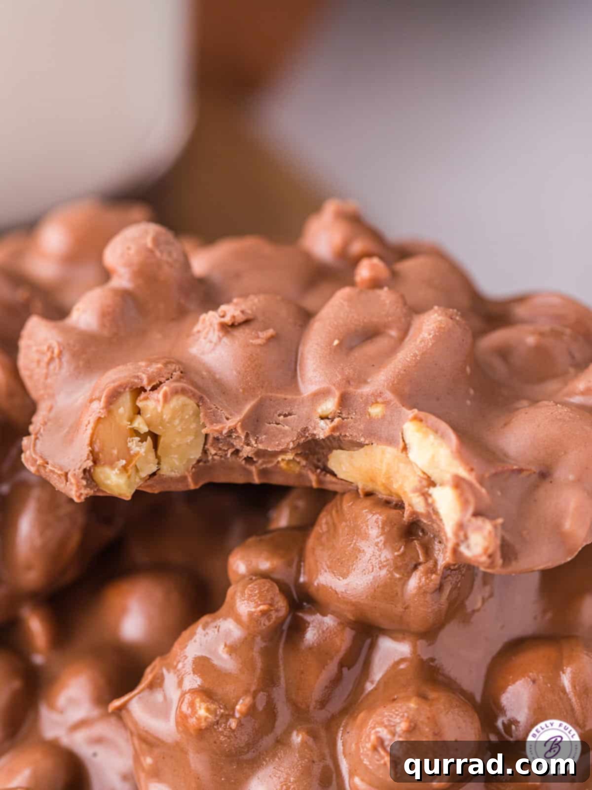 A close-up showing the irresistible texture of Crockpot Candy. A single piece of crockpot candy with a bite taken out, revealing its crunchy peanut interior.