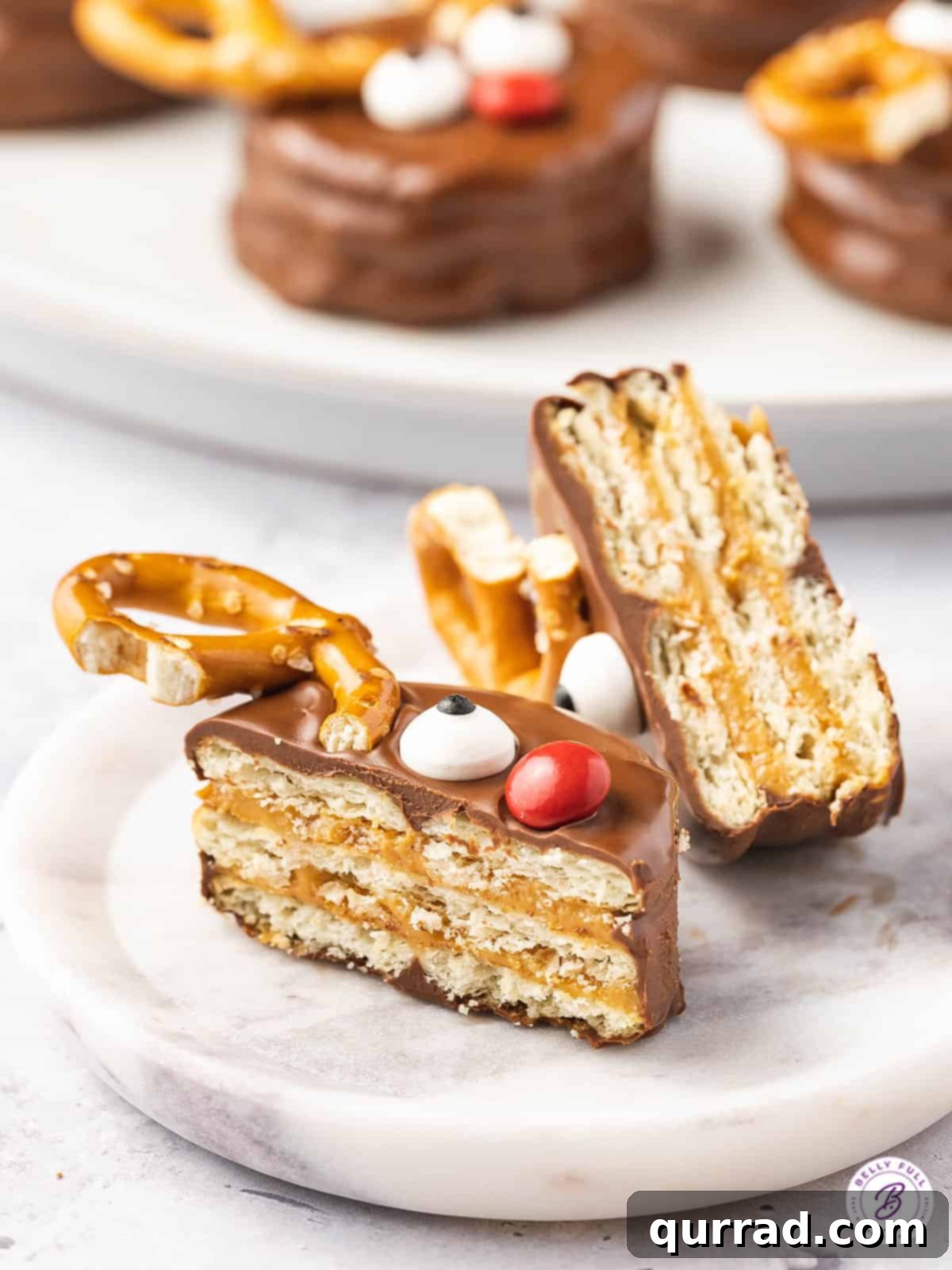 Festive Reindeer Ritz Treats 4 A Ritz cracker cookie cut in half, showcasing the creamy peanut butter filling, chocolate coating, candy eye, and red M&M nose.