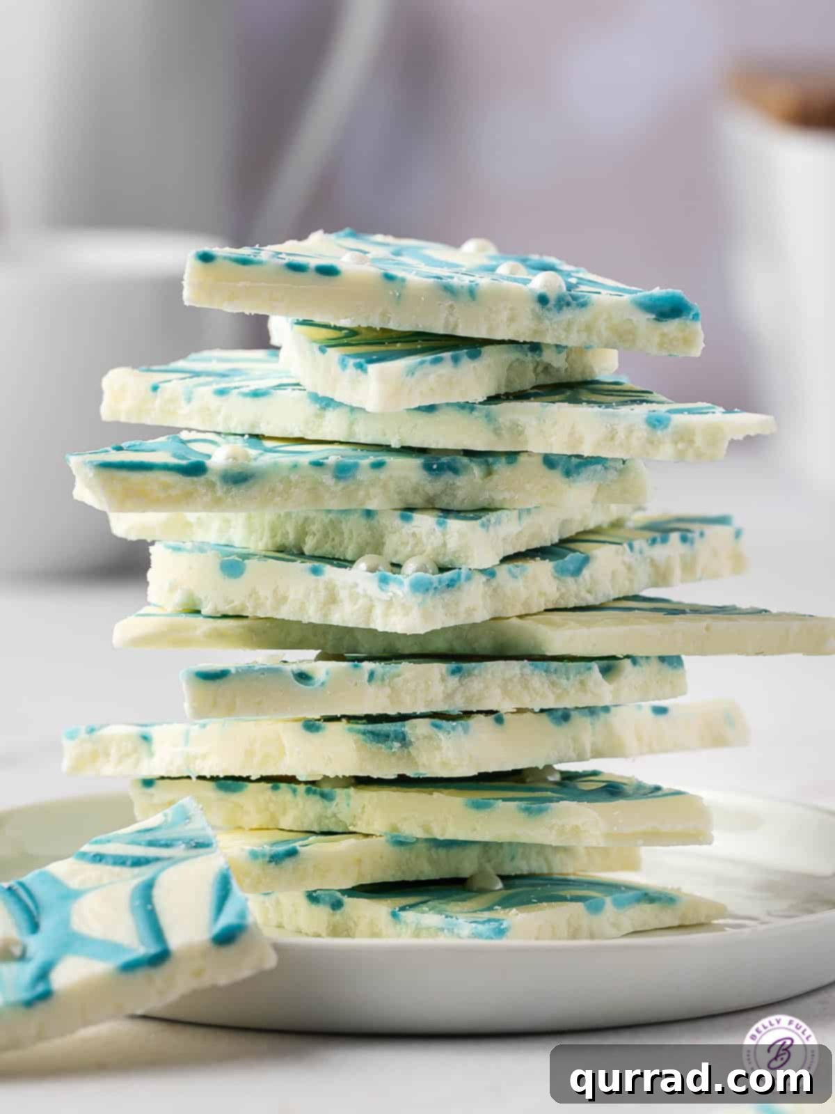 A tall stack of beautiful blue and white chocolate bark pieces, showcasing the marble effect and pearl sprinkles.