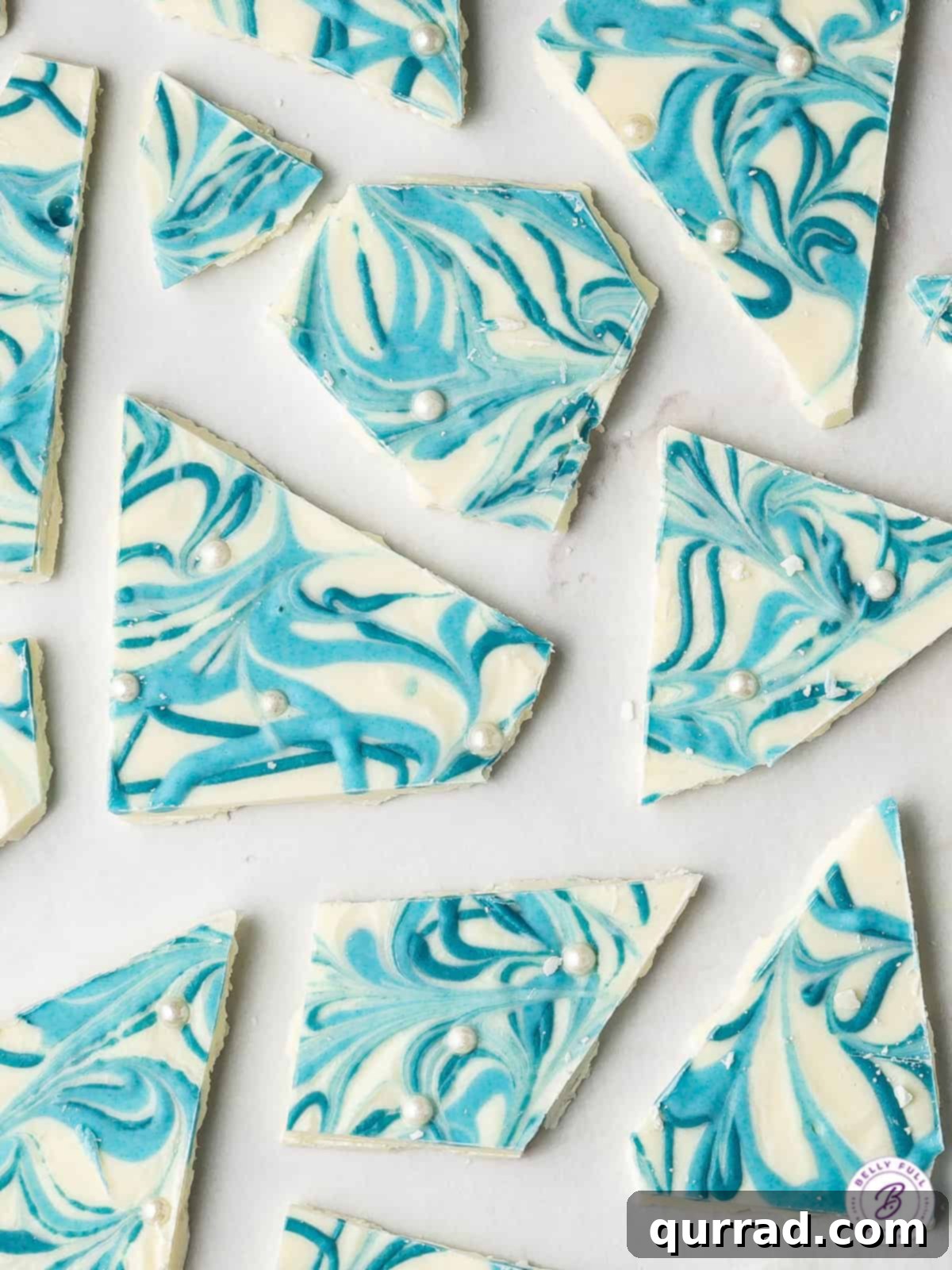 Overhead view of beautiful swirled blue and white chocolate bark pieces arranged on parchment paper, ready for gifting or serving.