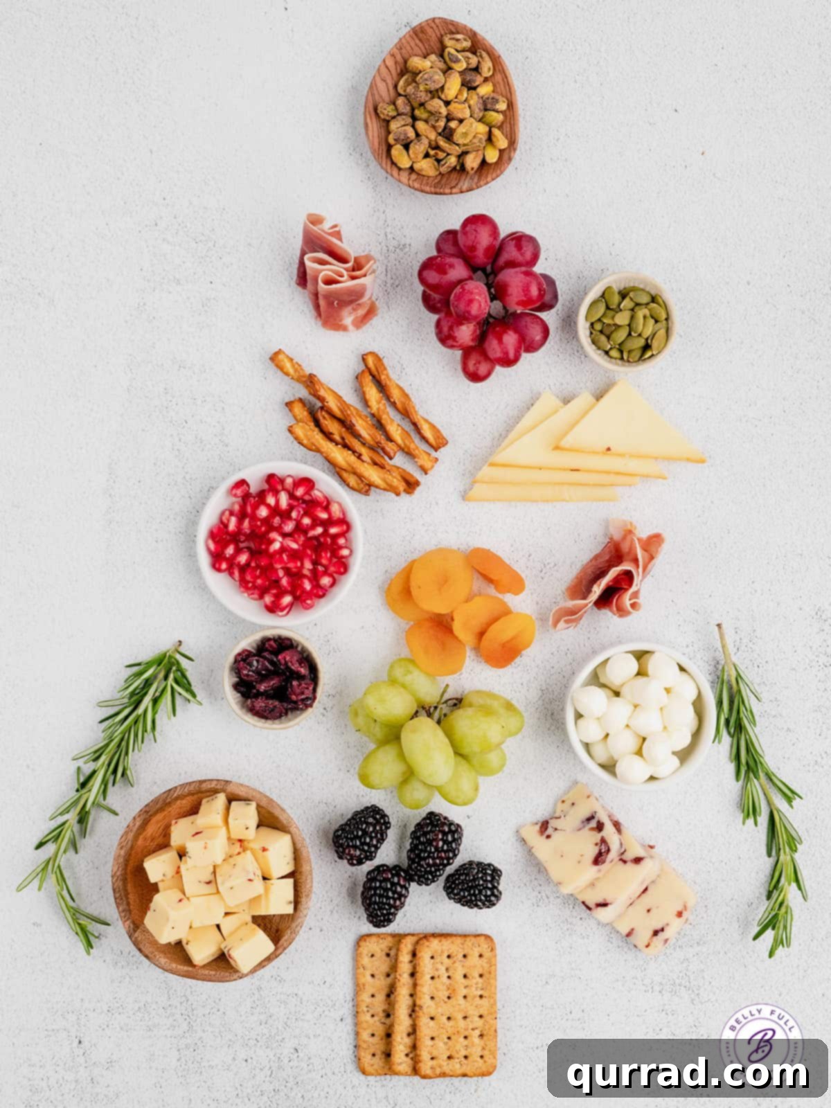 A vibrant display of fresh and dried fruits, gourmet cheeses, savory prosciutto, and nuts, ready to be assembled into a Christmas Tree Charcuterie Board. Overhead view of a variety of fresh ingredients laid out for a Christmas Tree Charcuterie Board, including different cheeses, grapes, berries, and nuts.