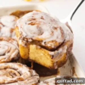 A spoon lifting out a cinnamon roll from a baking dish
