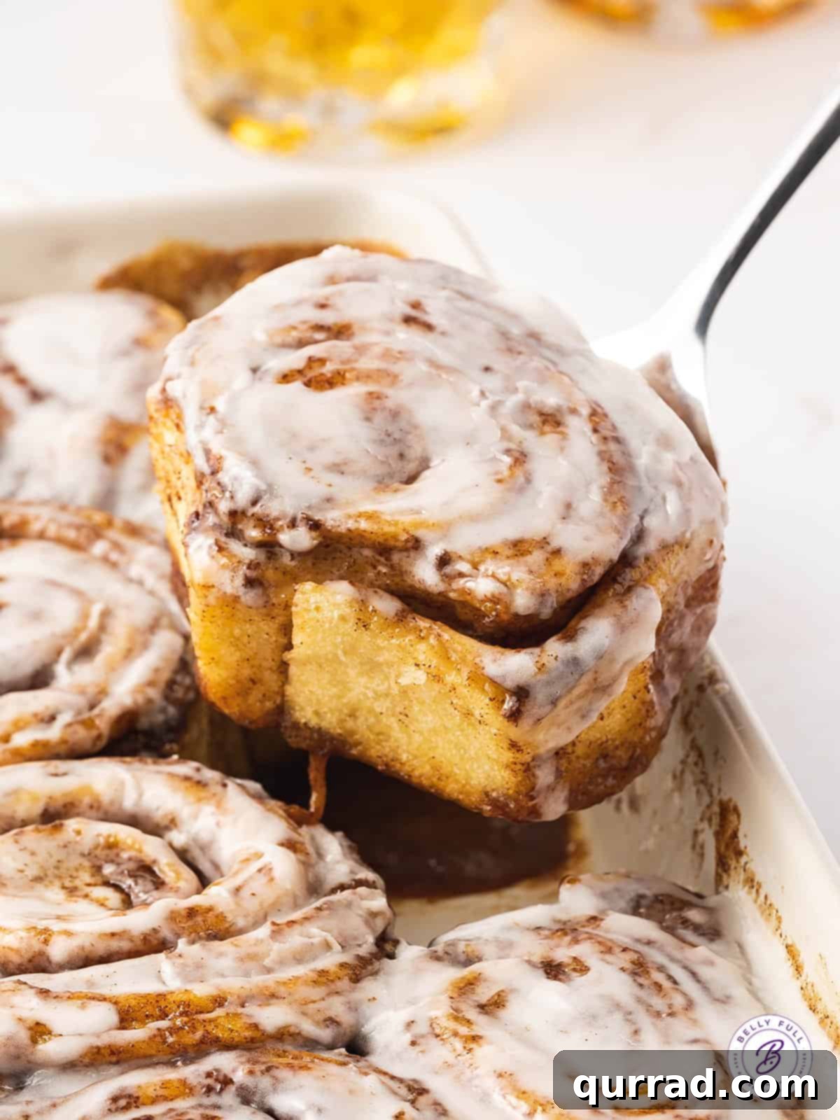 Foolproof Cinnamon Rolls 4 A spoon lifting out a cinnamon roll from a baking dish, showcasing its gooey center