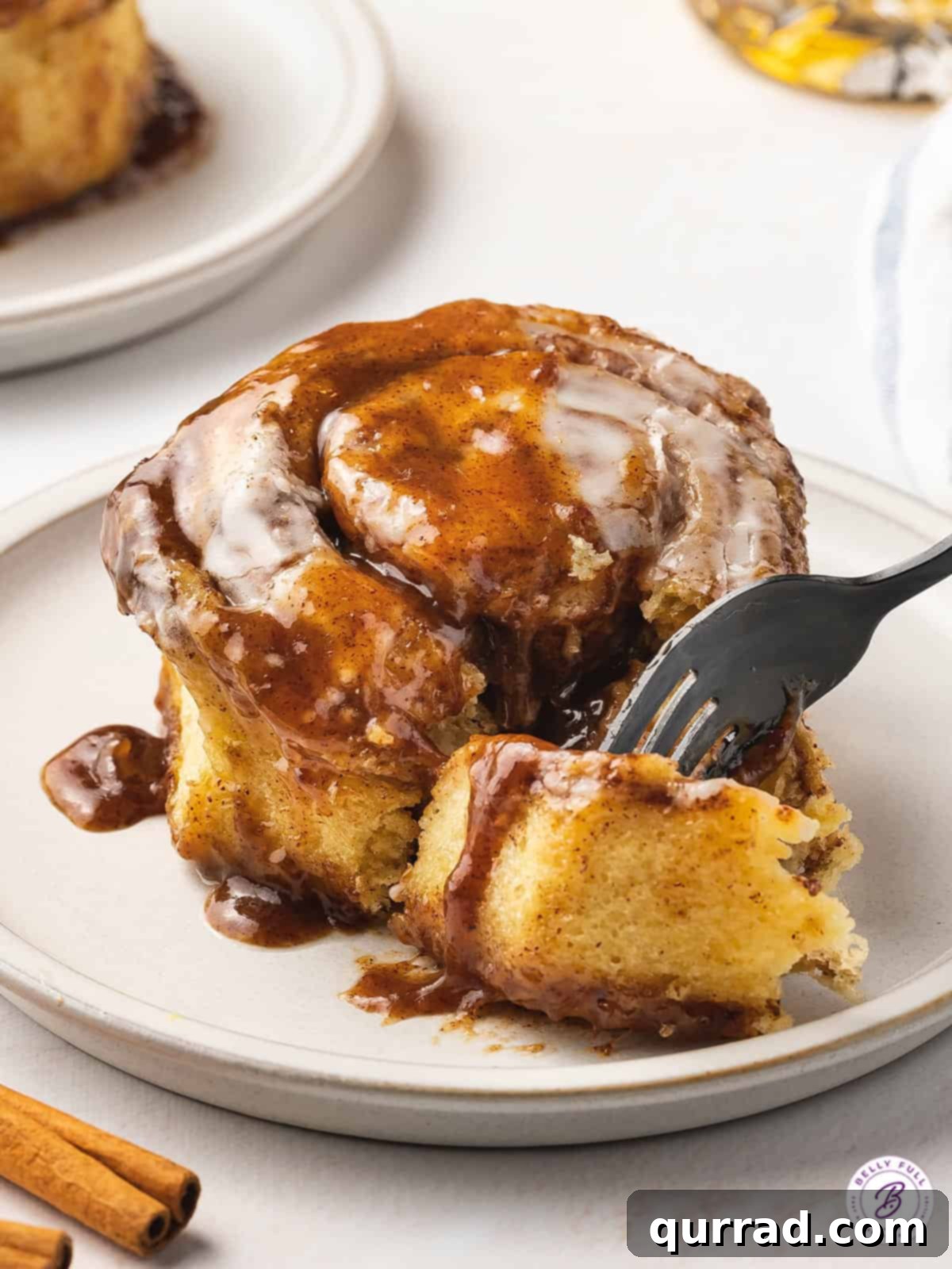 Foolproof Cinnamon Rolls 5 A fork diving into a cinnamon roll on a white plate, showing the soft interior