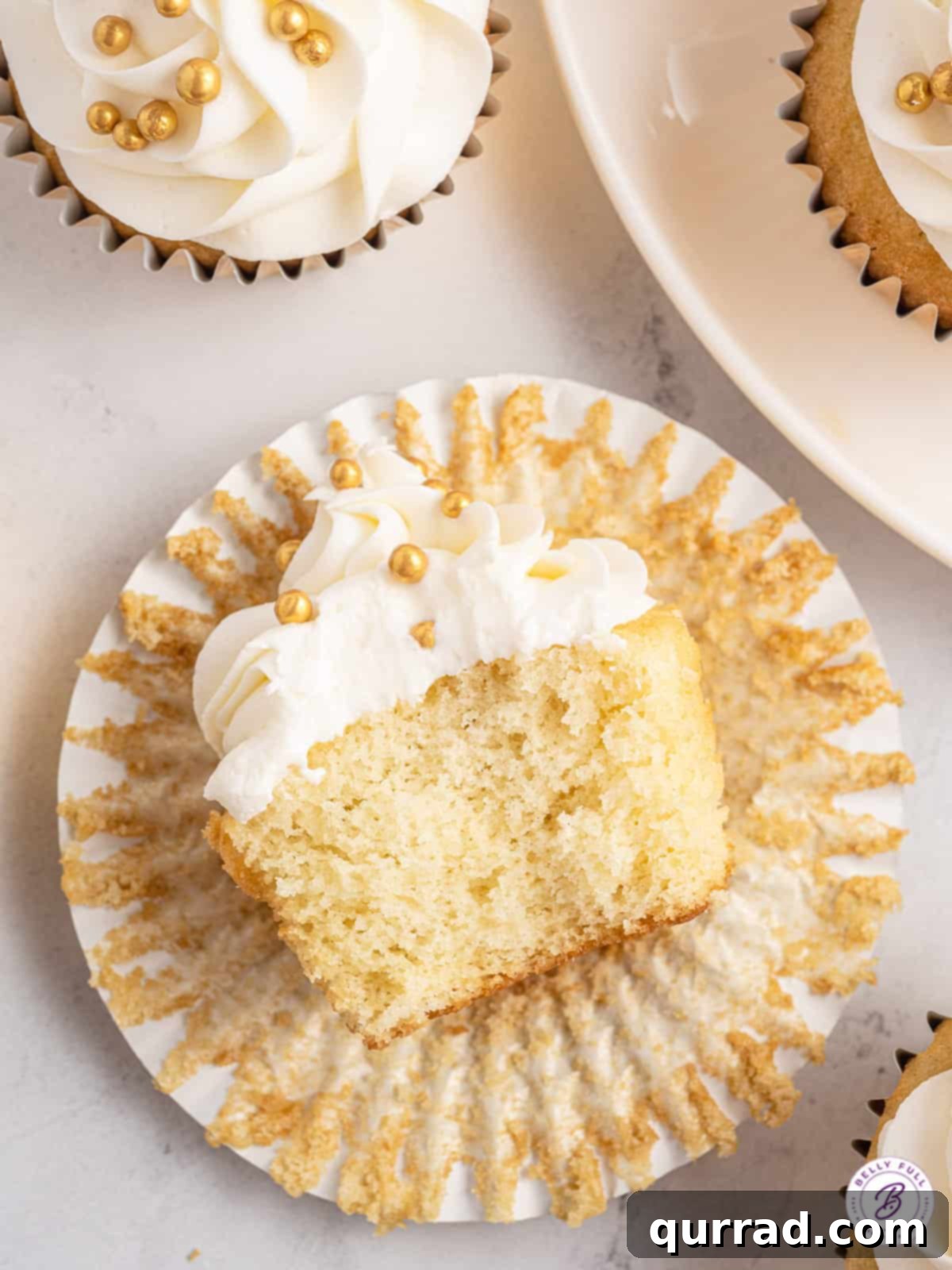 These moist, fluffy Prosecco Cupcakes are topped with a smooth buttercream frosting. An easy New Year's Eve dessert! A champagne cupcake cut in half, revealing its moist interior and light texture, resting on a wrapper.
