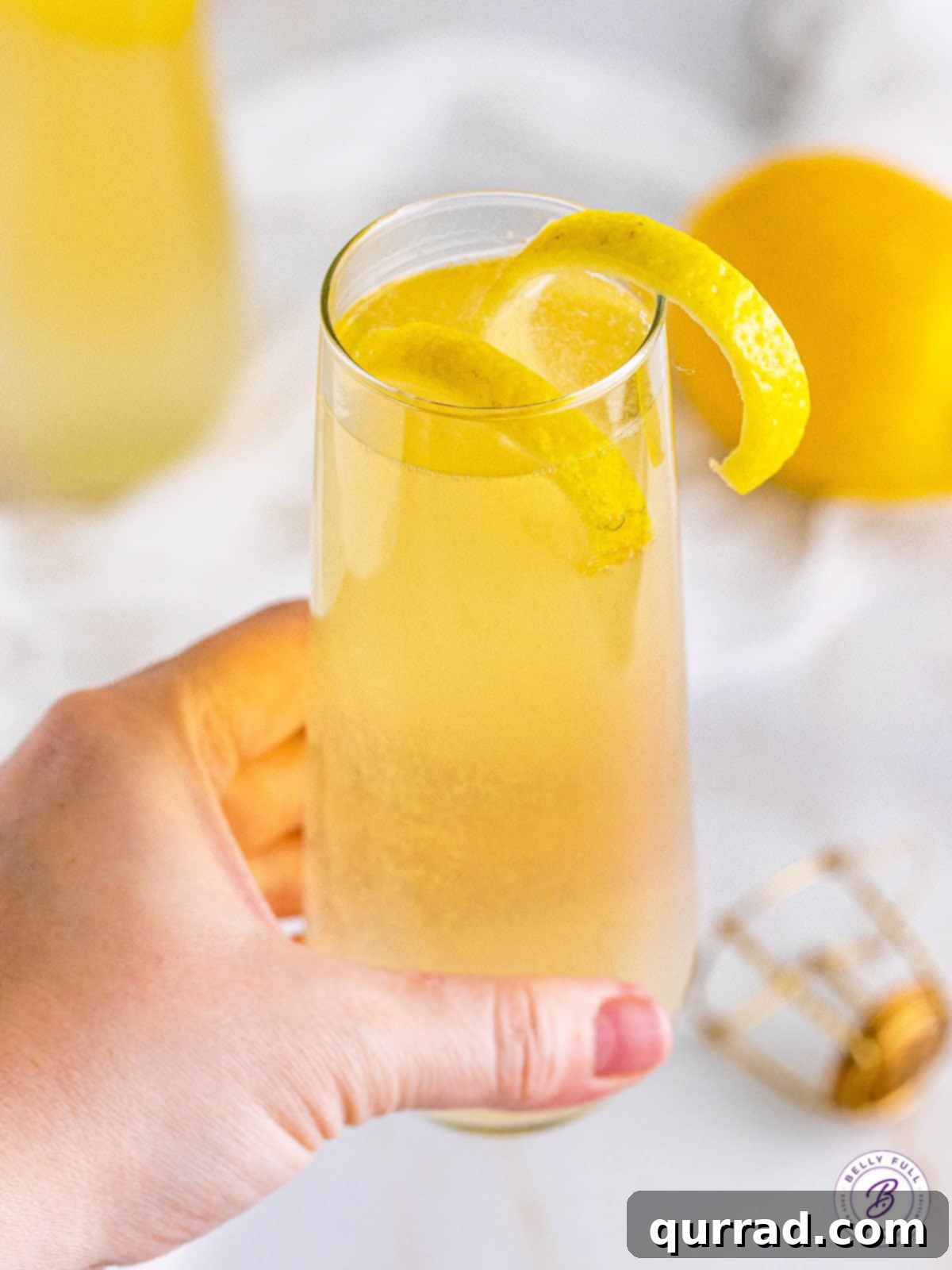 Made with gin, lemon juice, simple syrup, and champagne, this French 75 cocktail is easy to make and even easier to drink! A hand holding a French 75