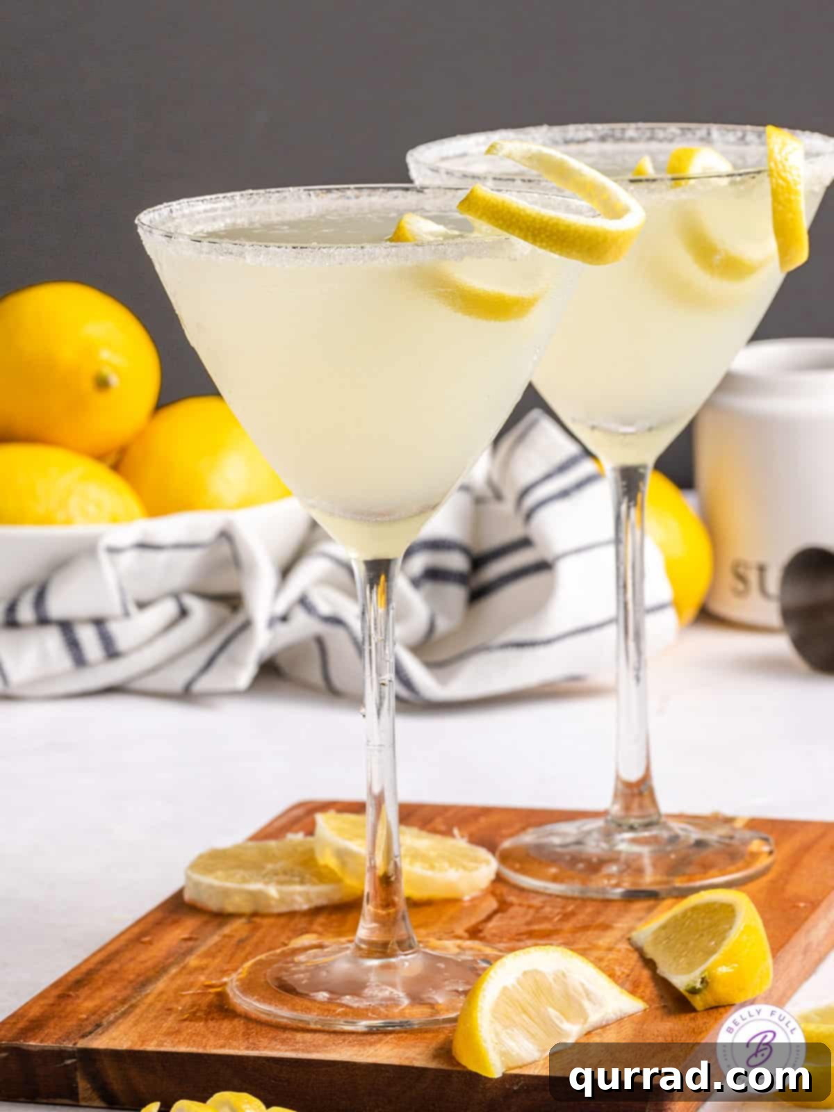 An easy-to-make, tart, and tangy Lemon Drop Martini, perfect for all special occasions and ready in minutes. Two perfectly prepared lemon drop martinis on a elegant wooden board, garnished with fresh lemon slices and a sugared rim, reflecting the warm ambient light.