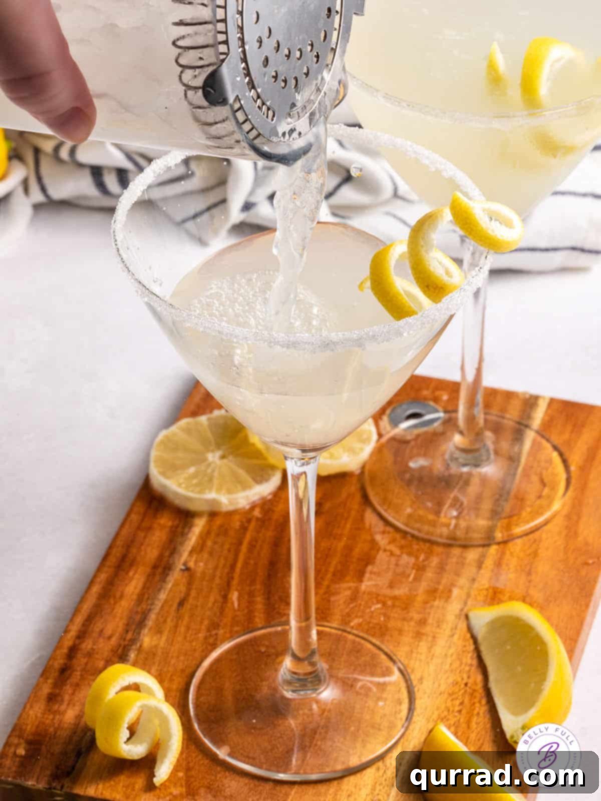 An easy-to-make, tart, and tangy Lemon Drop Martini, perfect for all special occasions and ready in minutes. A cocktail shaker pouring a vibrant yellow liquid into a martini glass with a sugared rim, highlighting the meticulous preparation of a Lemon Drop Martini.